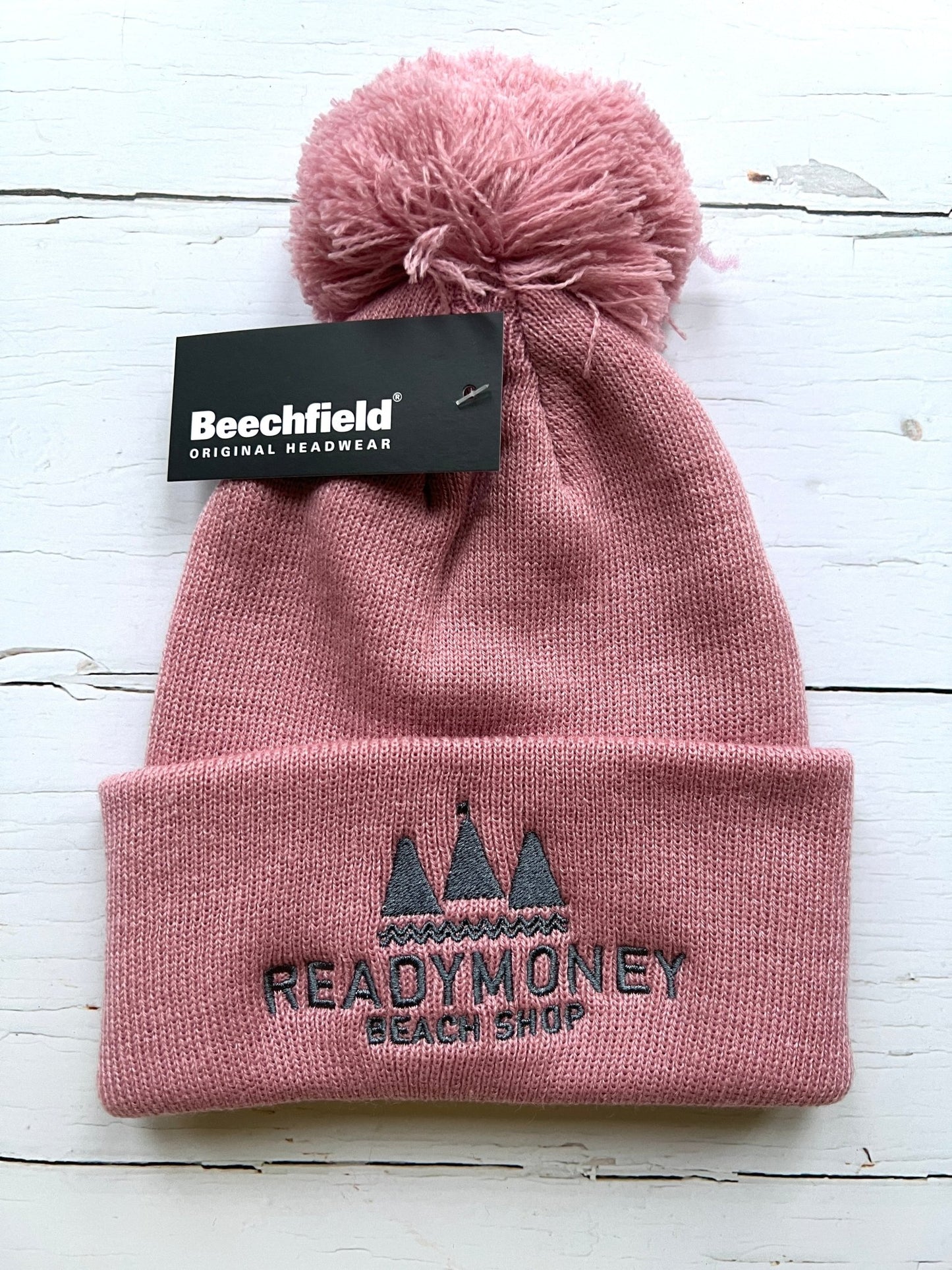 dusky pink kids’ beanie with pom-pom, soft knit, and embroidered beach shop logo—warm, playful, and coastal-chic
