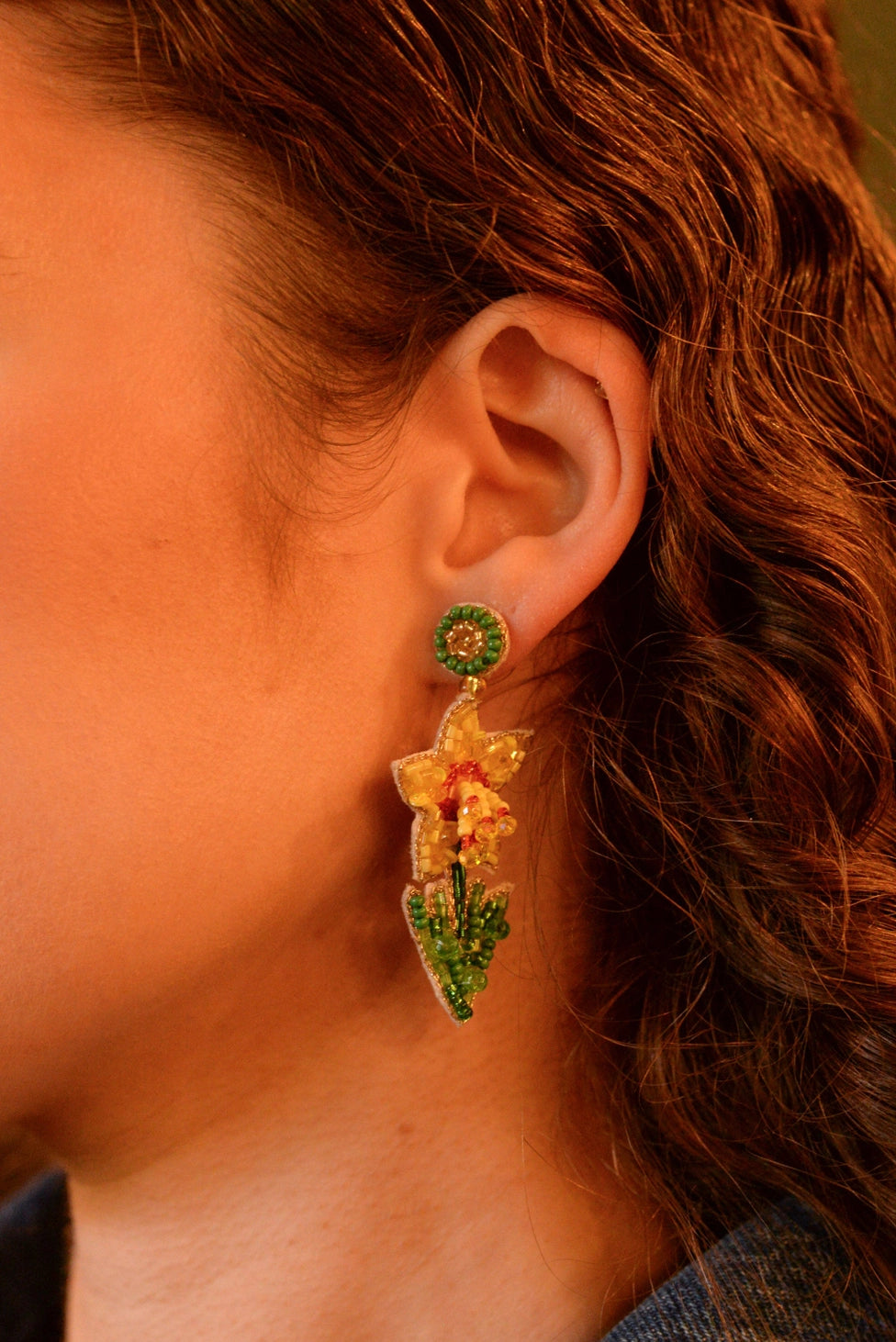 Close-up of a person wearing a floral earring with green and red details.