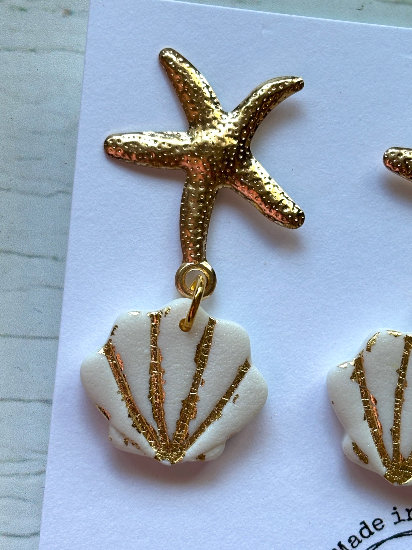 closeup shot of gold starfish earring stud connected to a white seashell dangle handmade polymer resin and gold-tone jewelry