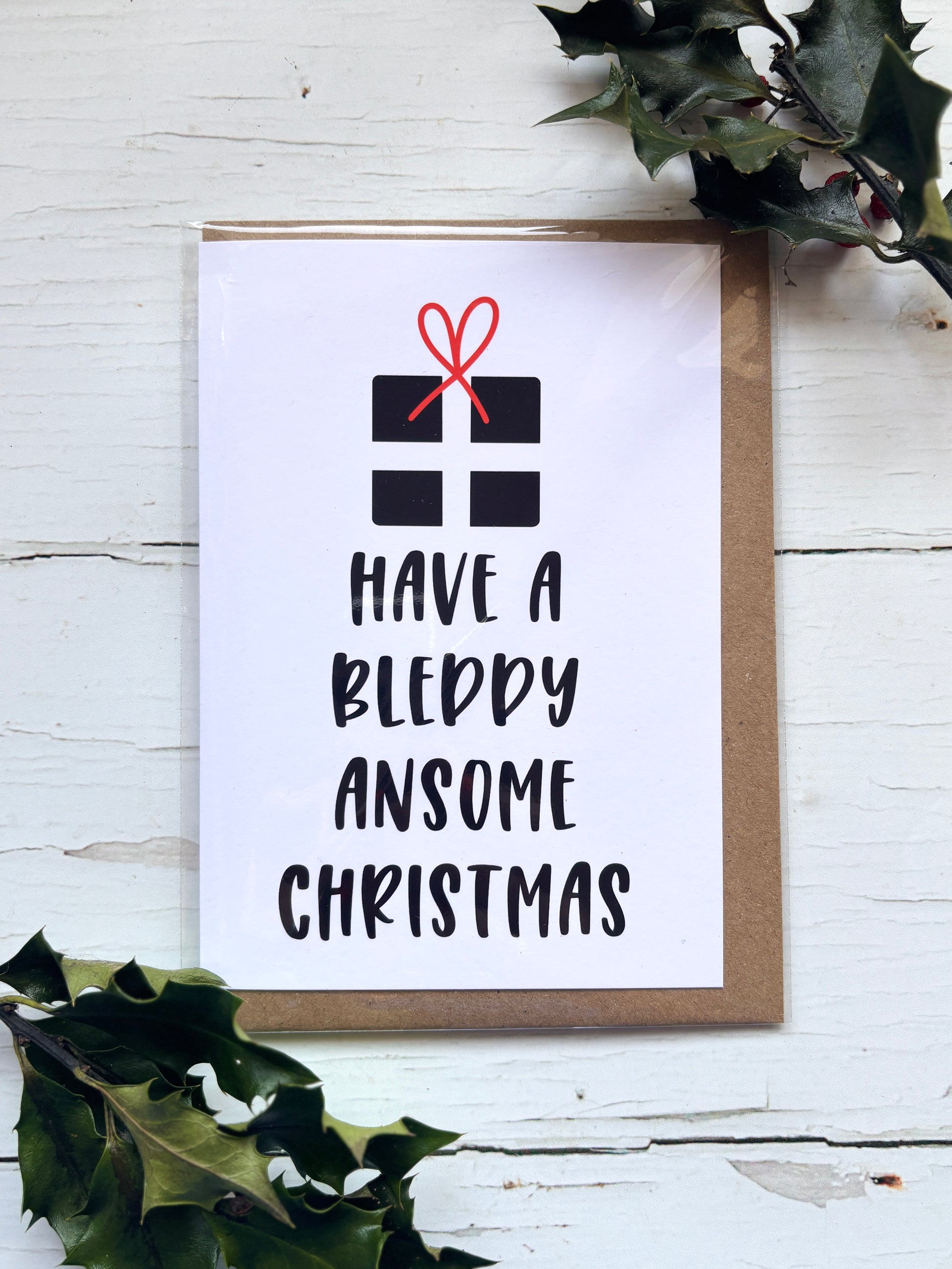 Funny Cornish Christmas card with gift illustration and text “Have a Bleddy Ansome Christmas,” festive holiday greeting design