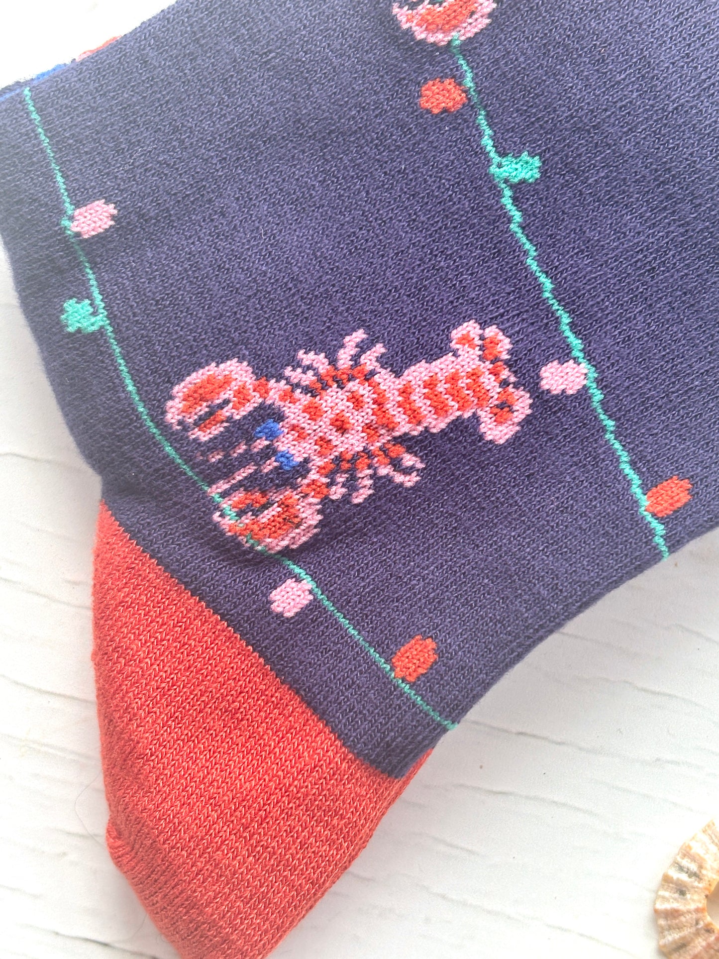 closeup shot of Christmas socks navy bamboo knit with a woven pink lobster and string of colorful lights red toe and heel