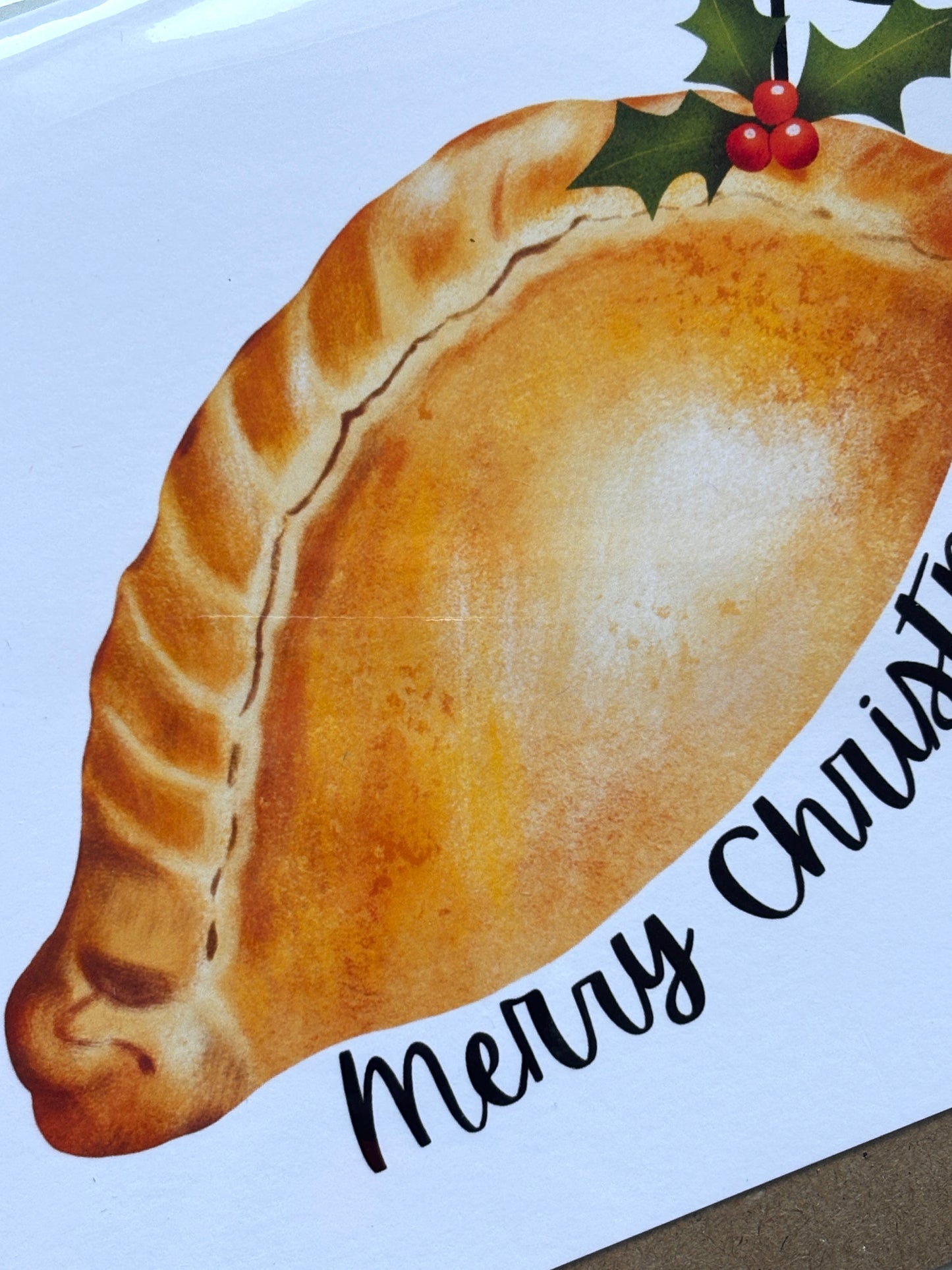 closeup shot of Cornish Christmas card with golden pasty, holly sprig, festive crust detail, and partial “Merry Christmas” greeting