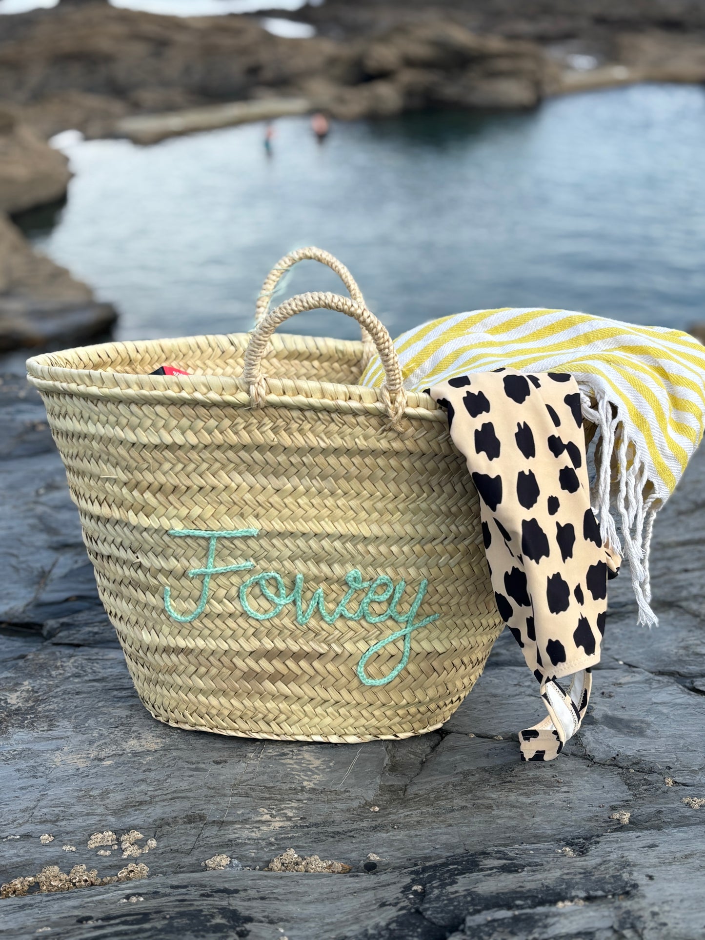 straw maxi basket with Fowey seafoam embroidery chic beach tote or coastal holiday bag set on rocks near the sea
