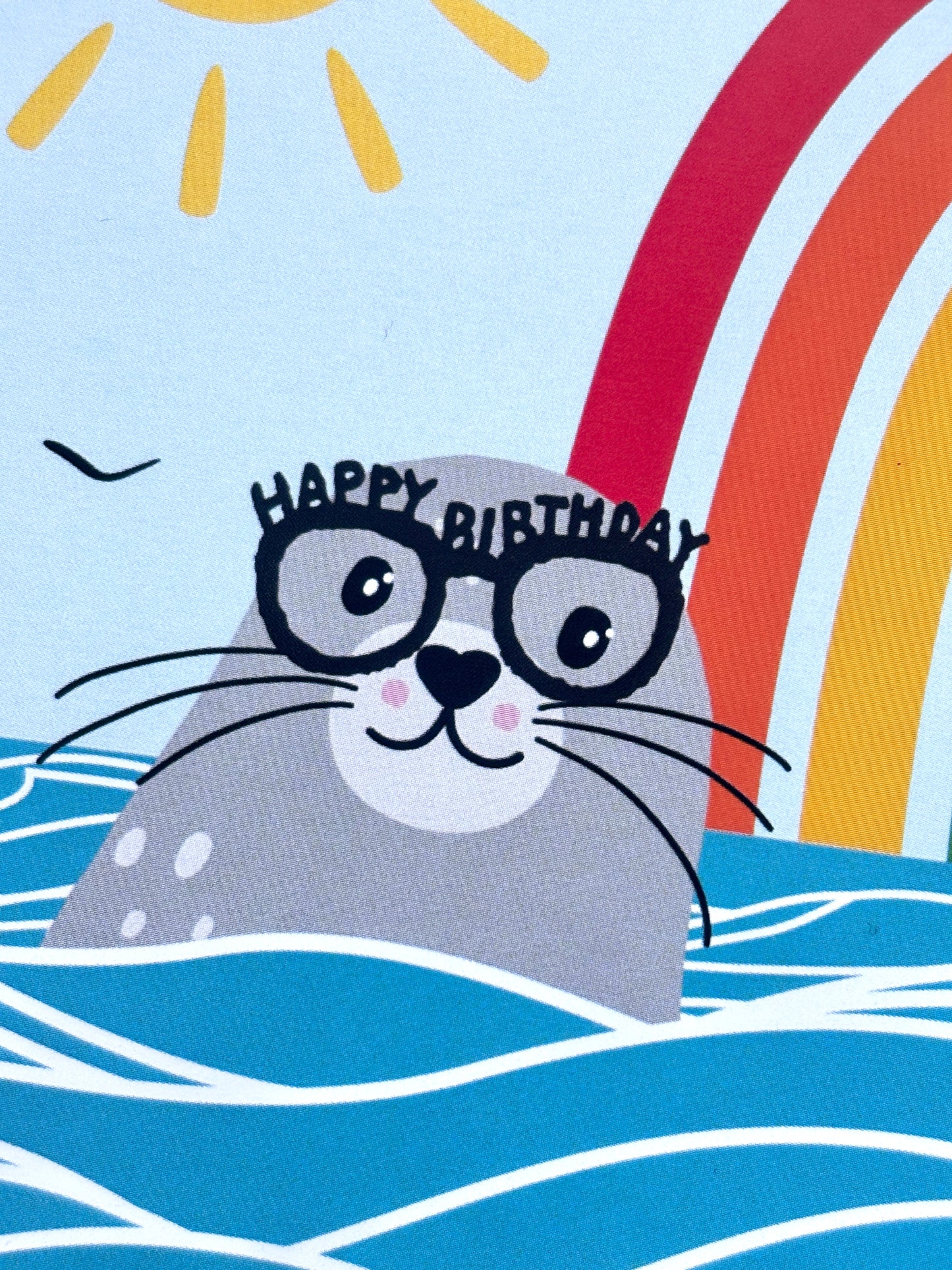 closeup shot of an adorable seal wearing Happy Birthday glasses, colorful rainbow detail, cheerful ocean-themed birthday card design