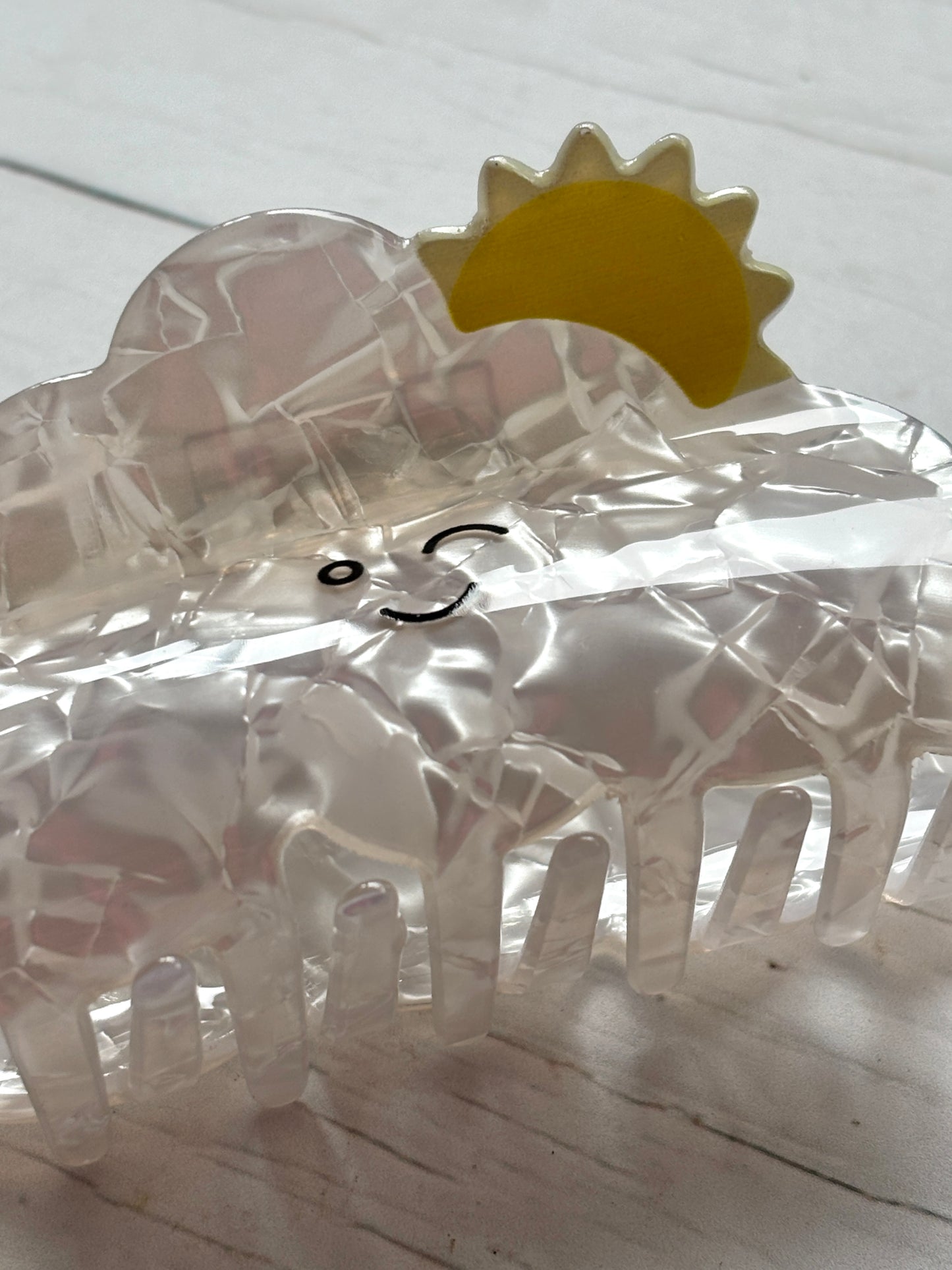 closeup shot of the happy cloud hair claw clip showing the winking face, yellow sun detail, and strong gripping teeth kawaii hair accessory