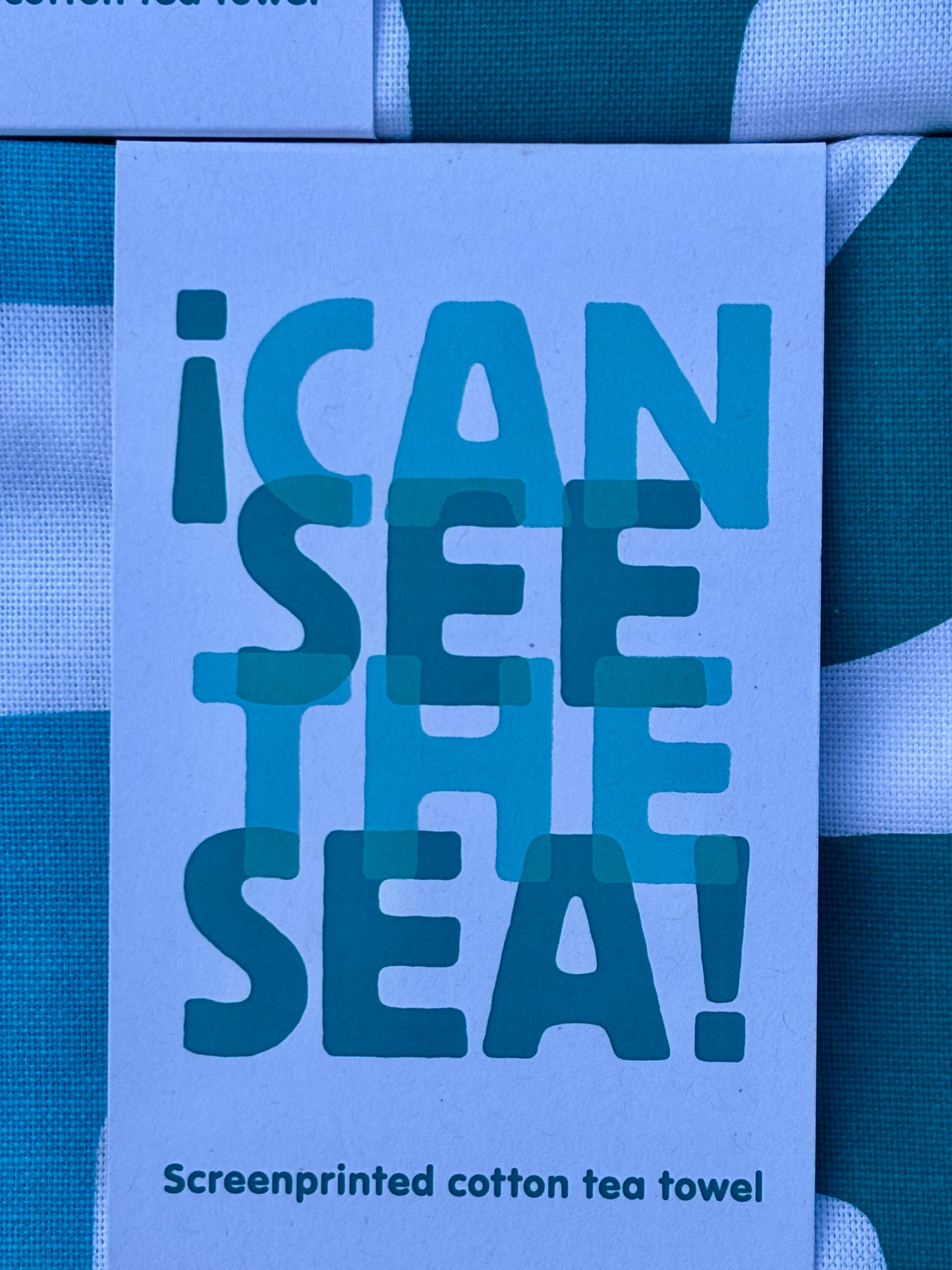 closeup shot of a "I Can See The Sea!" screenprinted cotton tea towel label abstract block design in teal and blue shades nautical kitchen linen detail