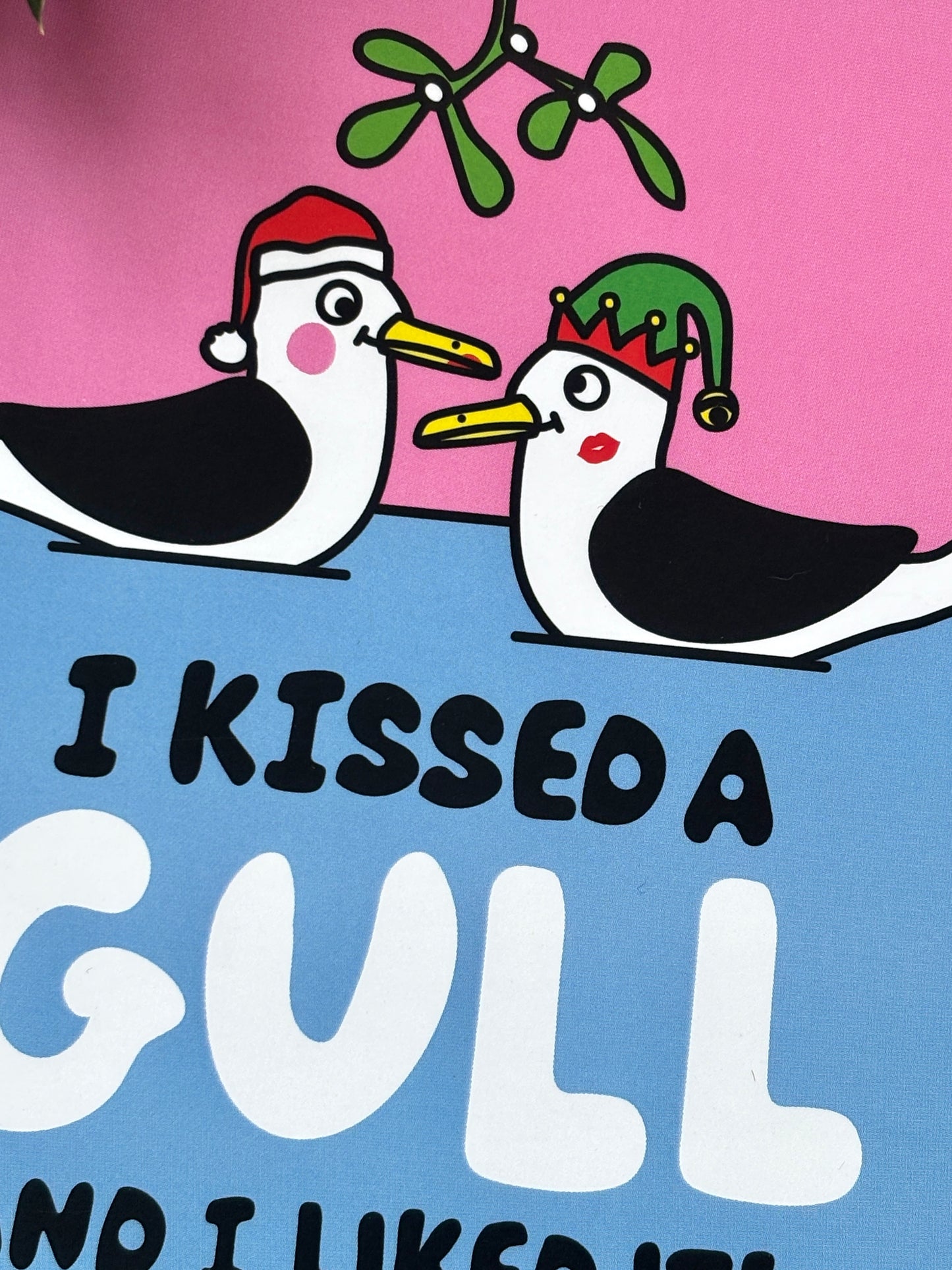 closeup shot of quirky Christmas card featuring kissing gulls under mistletoe, bold festive illustration, humorous coastal holiday design