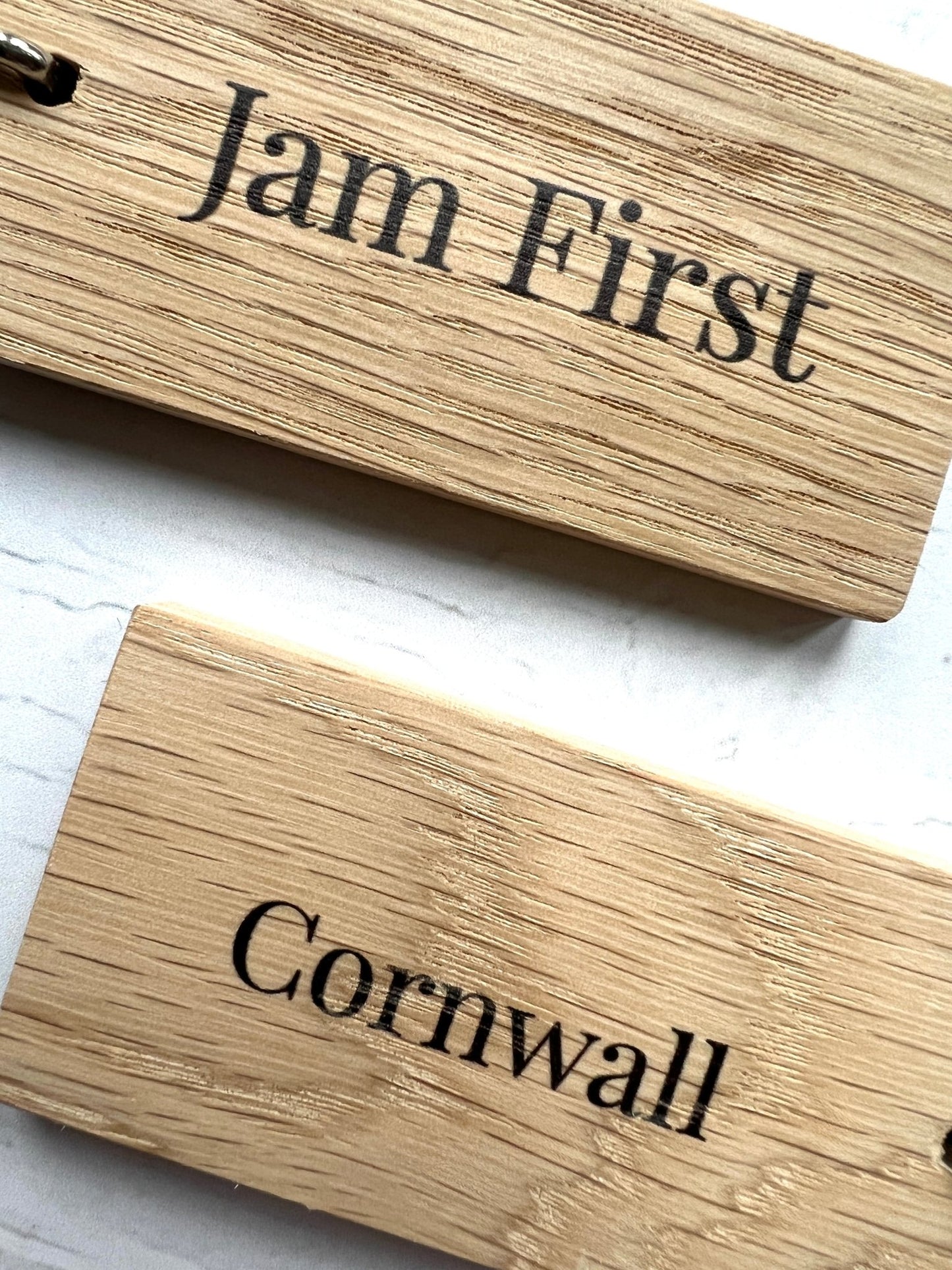 closeup shot of engraved wooden key rings with “Jam First” and “Cornwall”—handmade coastal accessories for cream tea lovers