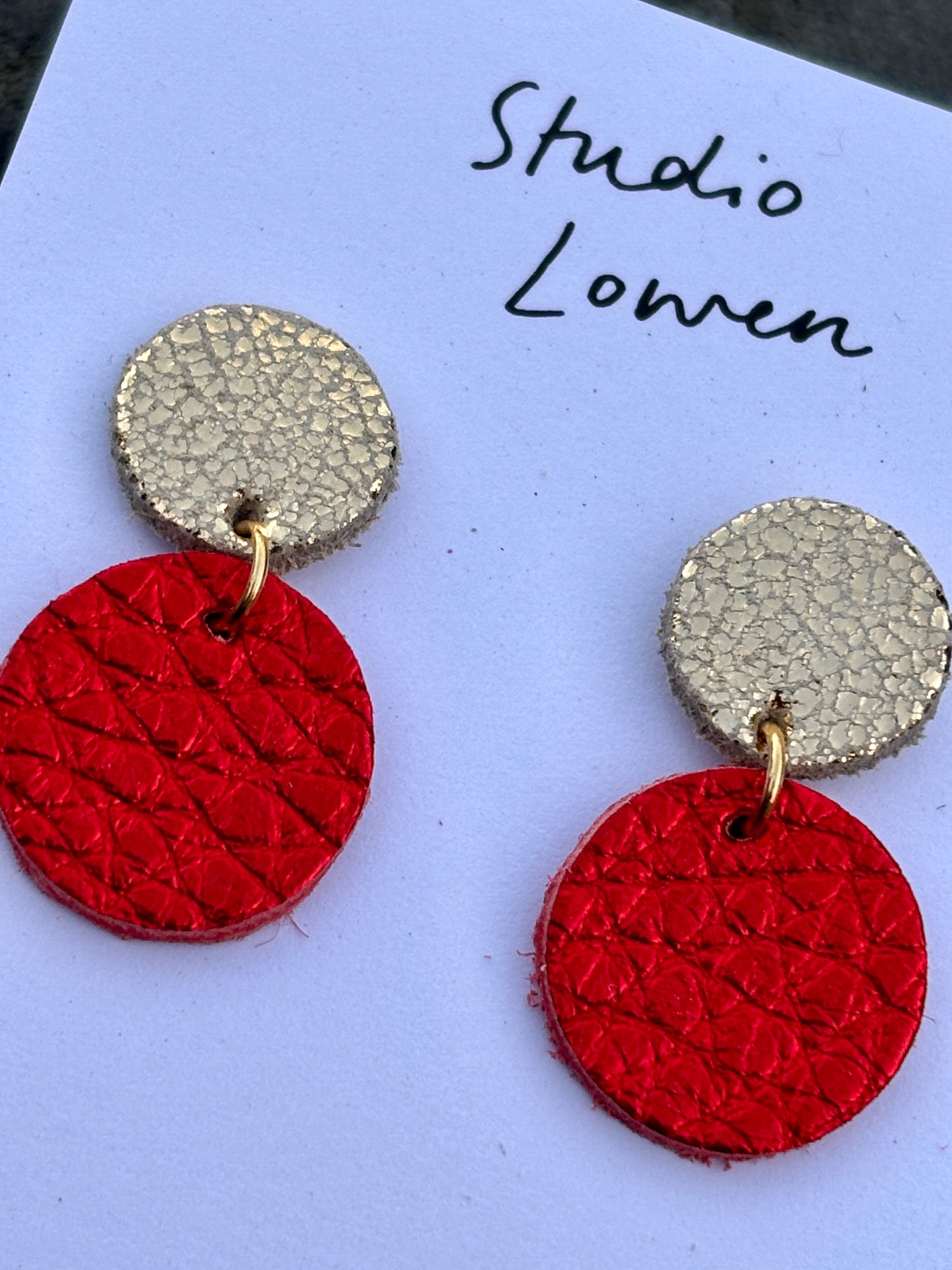 closeup shot of metallic red leather drop earrings—handmade, gold-detailed, textured holiday studs with bold festive flair