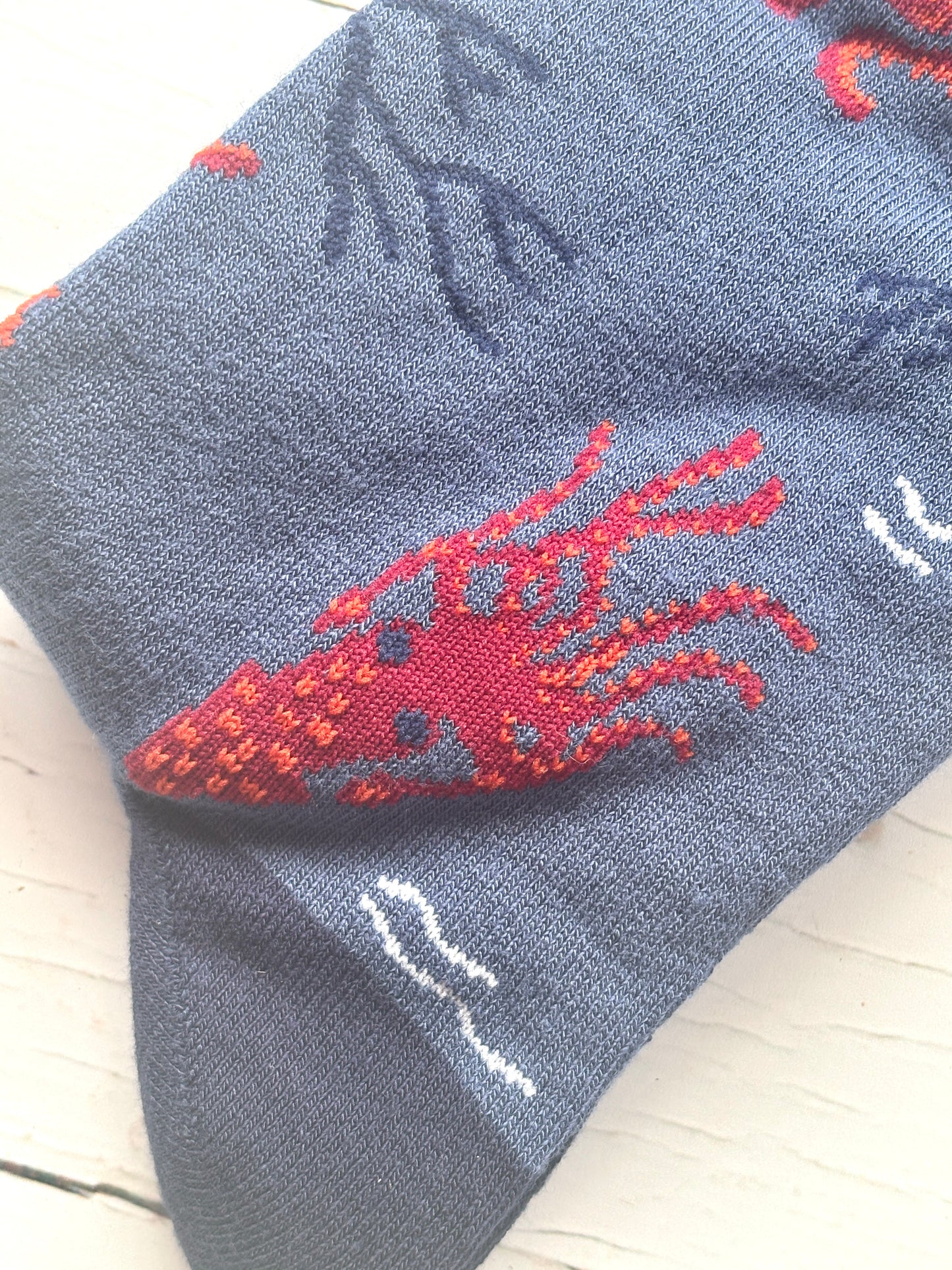 closeup shot of detail on a men's bamboo sock red octopus with orange accents, blue seaweed, and knitted texture coastal novelty gift