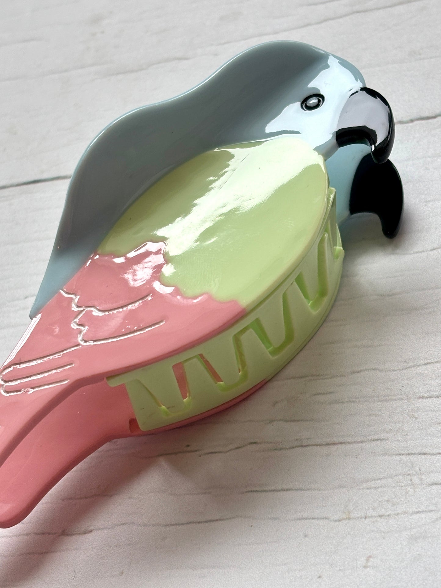 closeup shot of pastel parrot hair claw—colorful beak-to-tail clip with glossy finish and secure grip for tropical styling