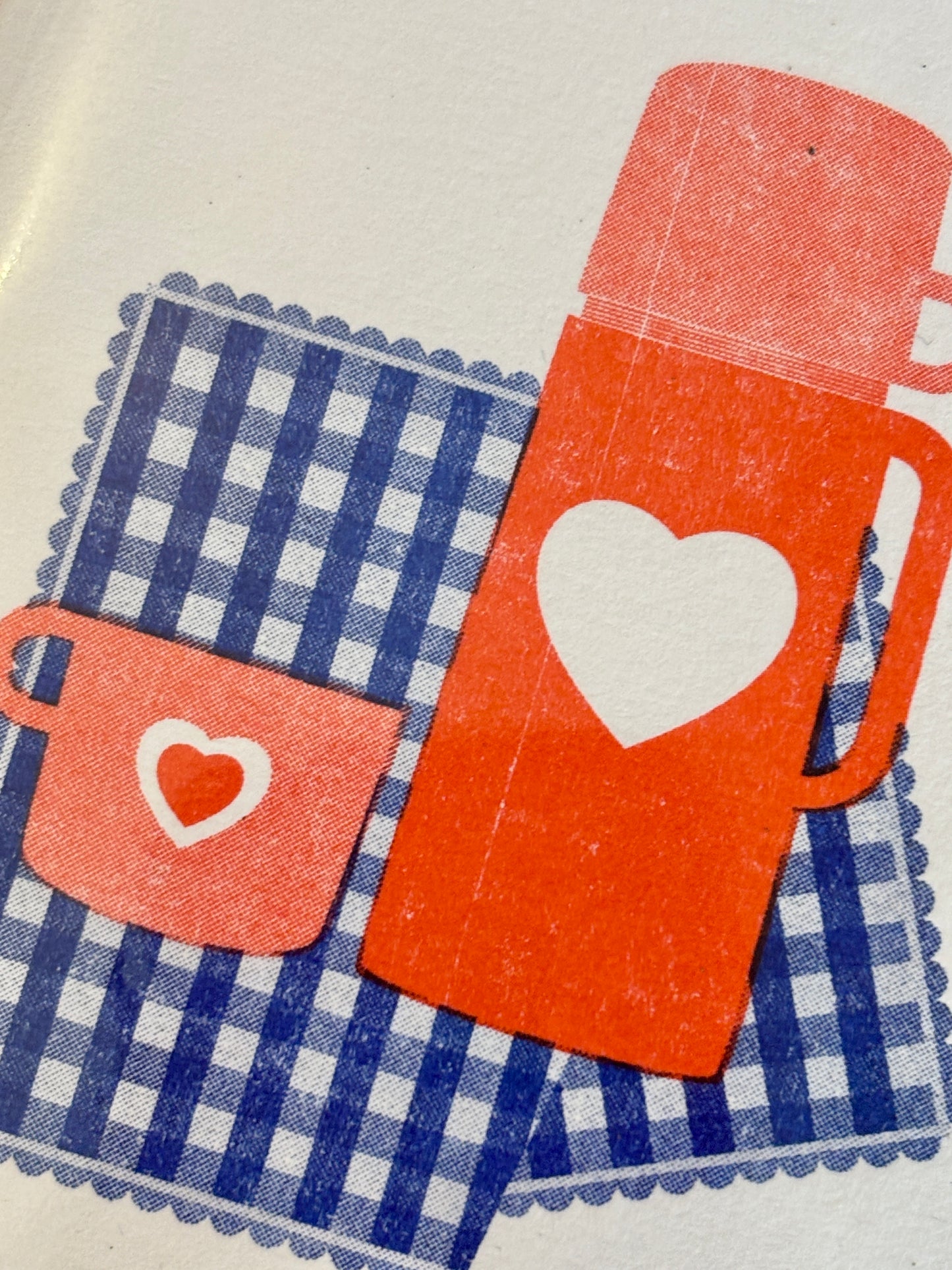 closeup shot of mini card illustration red thermos and mug with hearts on a blue gingham blanket romantic, beach, love note