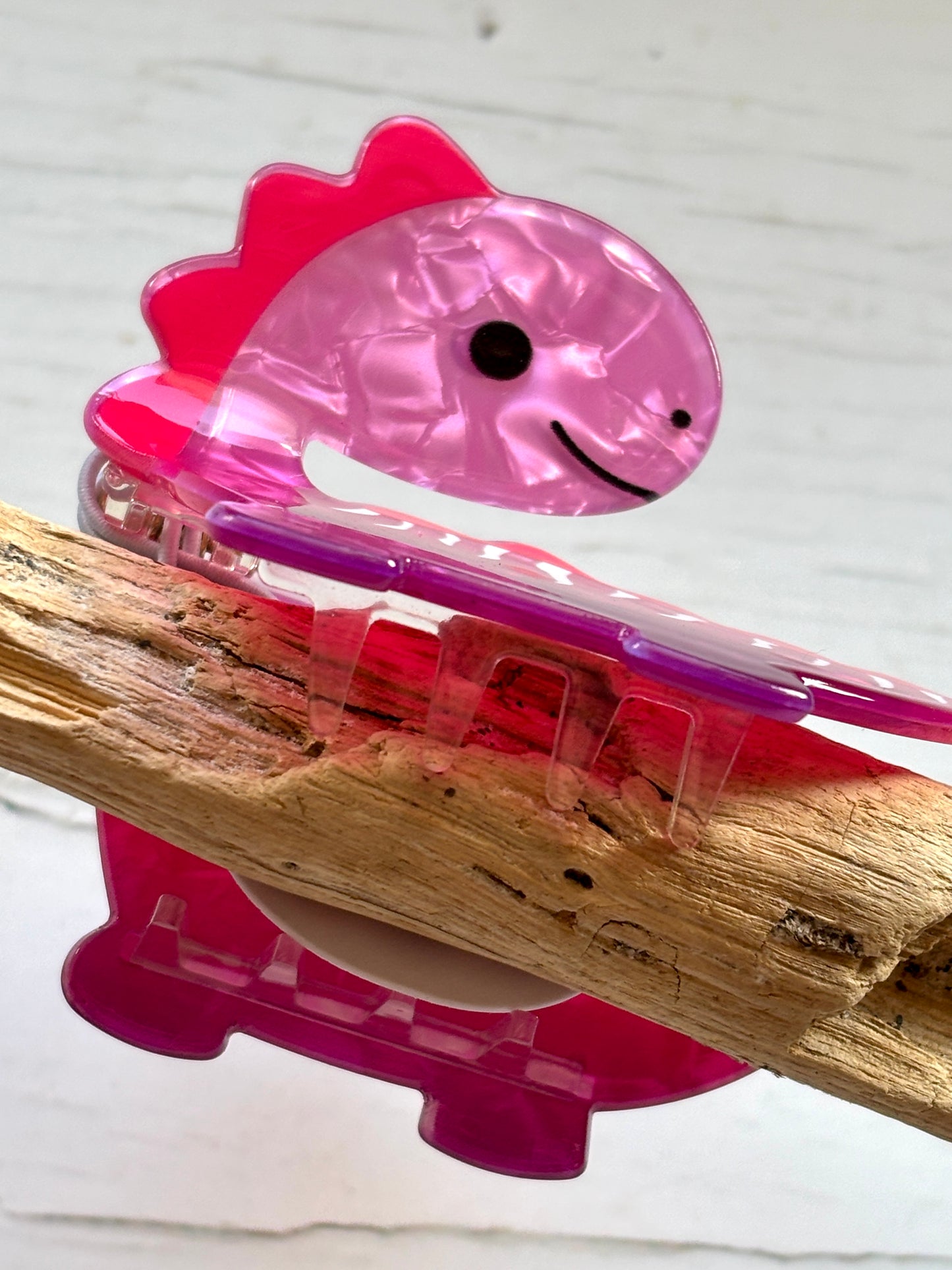 closeup shot on a marbled pink acrylic dinosaur novelty hair claw funky statement hair accessory or cute dino hair decor on driftwood
