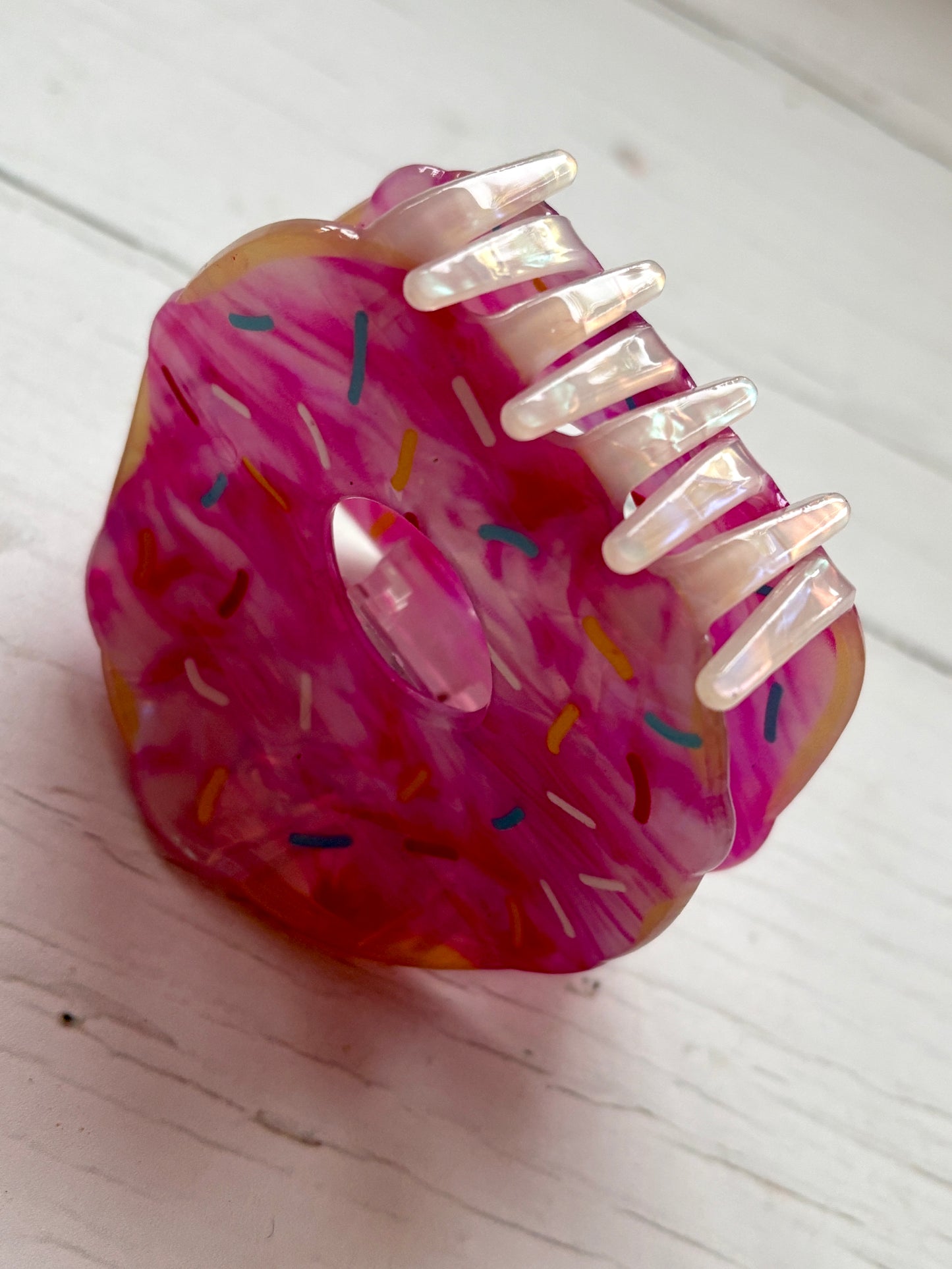 angled closeup shot of the pink doughnut hair claw clip, showing the iridescent teeth and colorful sprinkle detail on the acrylic frosting