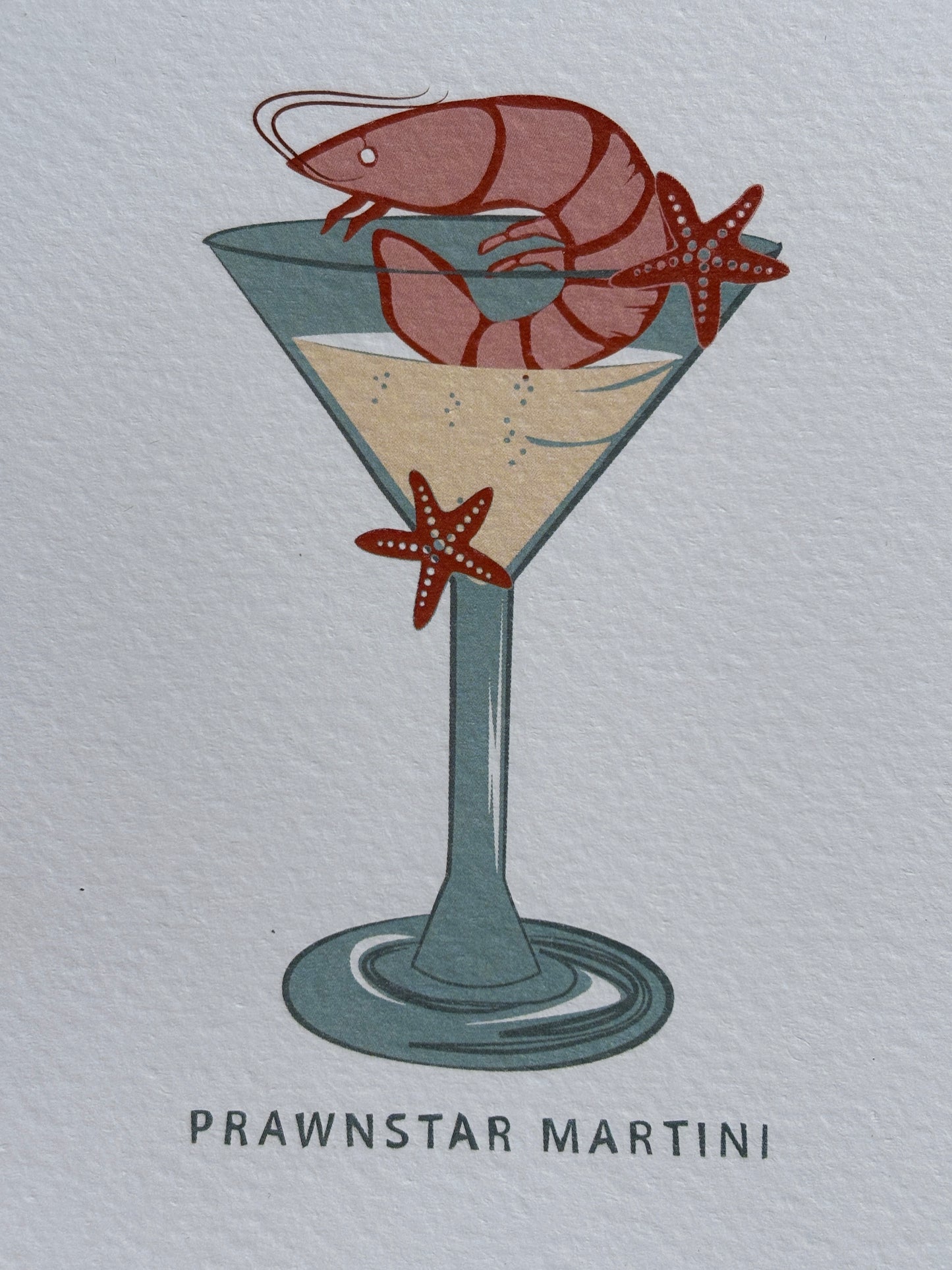 closeup shot of prawnstar Martini greeting card—quirky prawn and starfish cocktail illustration on textured paper, ideal for coastal humor and gifting