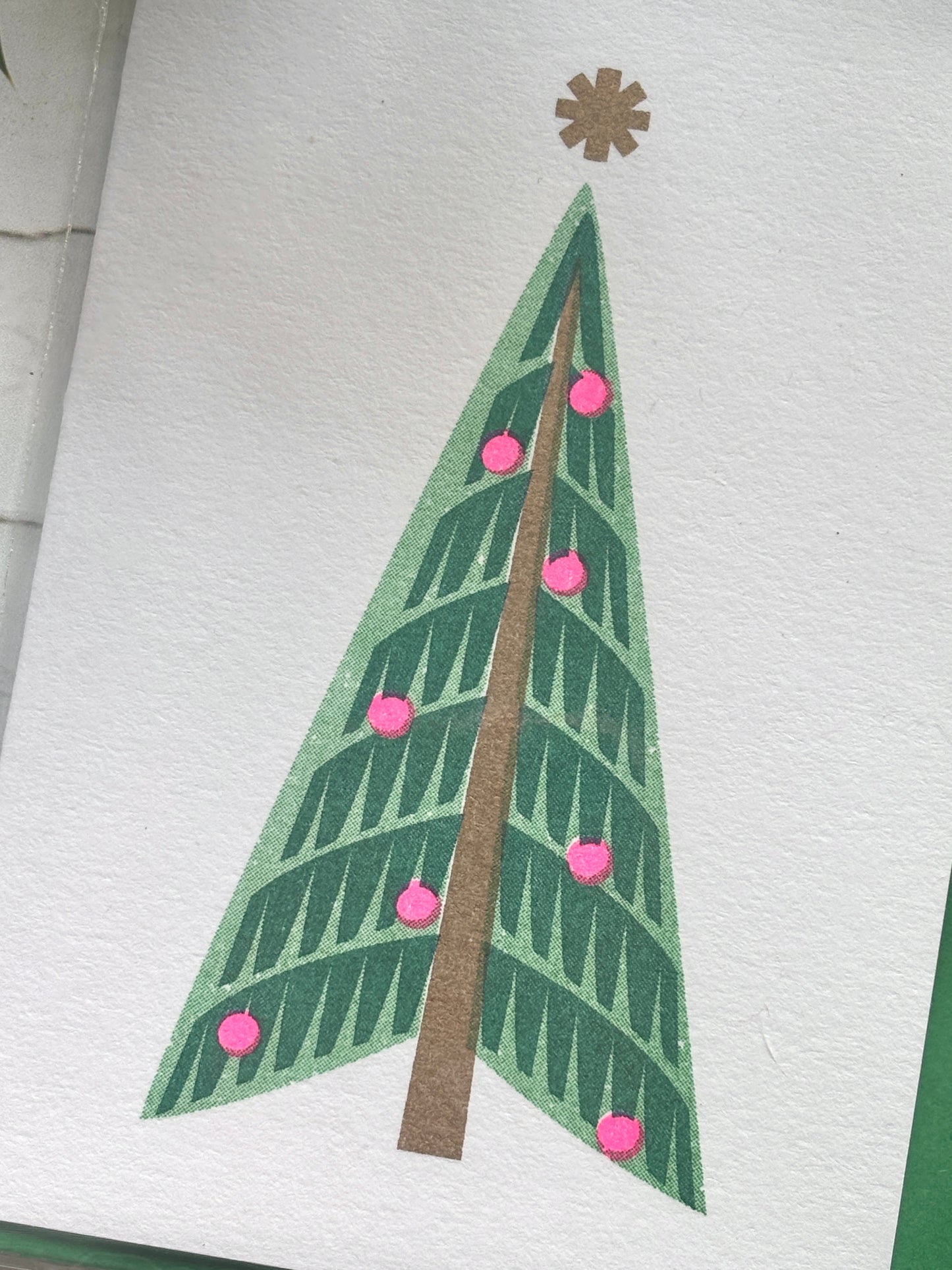 closeup shot of retro style Christmas card with minimalist green tree, pink baubles, and gold star, festive modern design