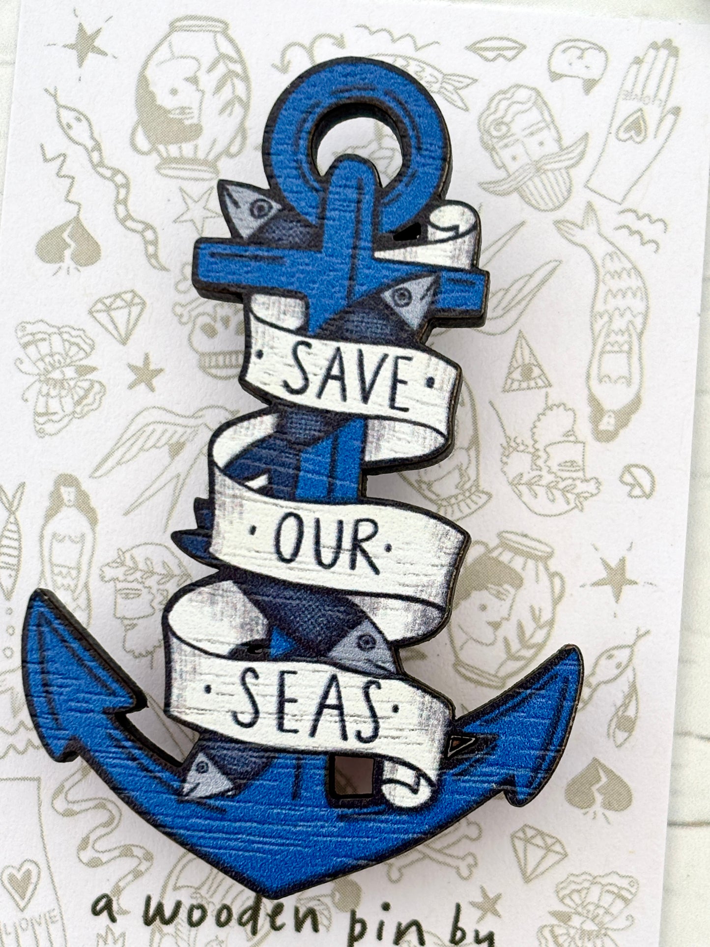 closeup shot of blue anchor wooden pin with “Save Our Seas” ribbon, eco-conscious ocean-themed accessory gift