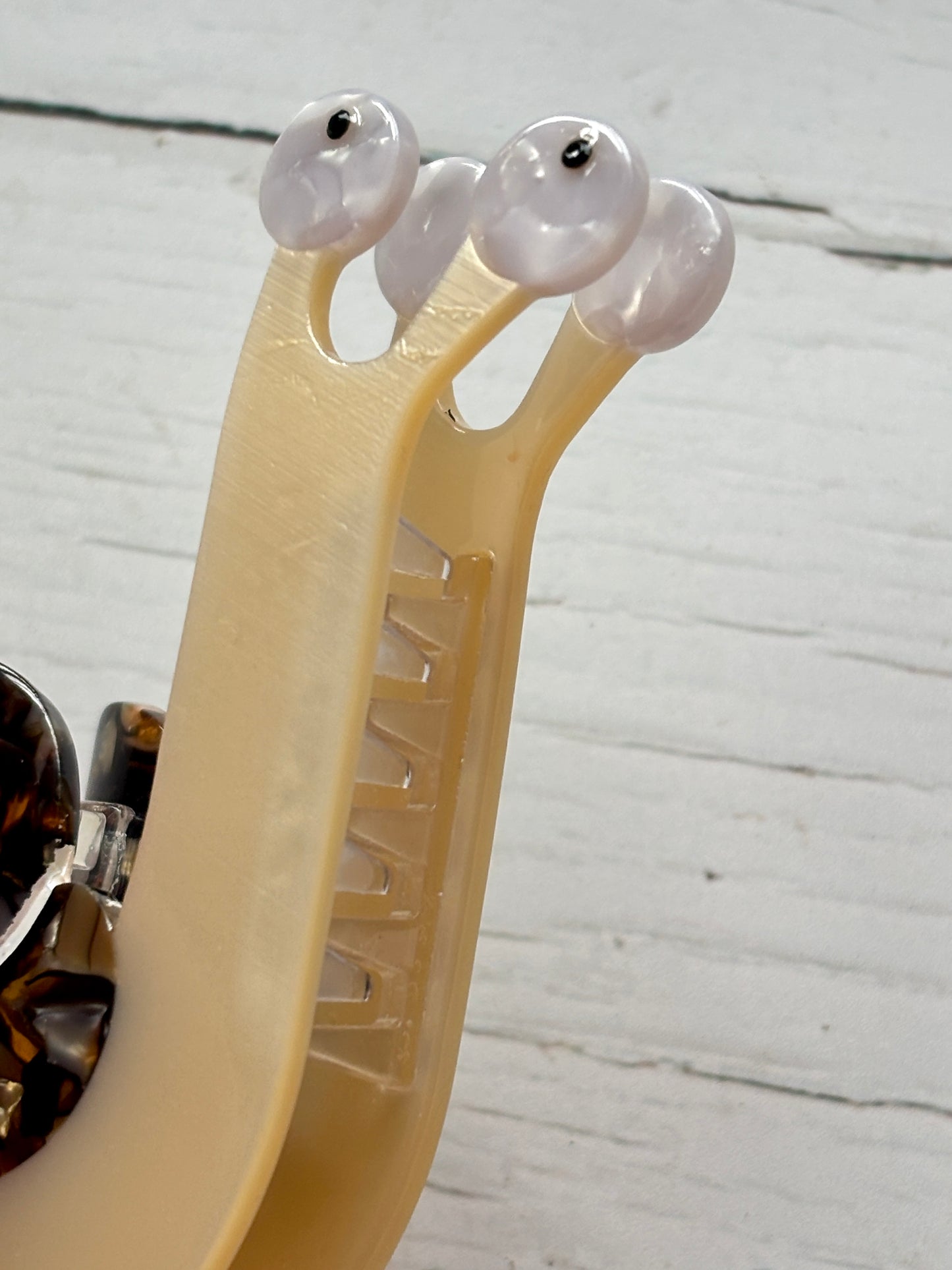 closeup shot of snail hair claw—beige clip with quirky eye stalks, tortoiseshell accents, and secure grip for playful styling