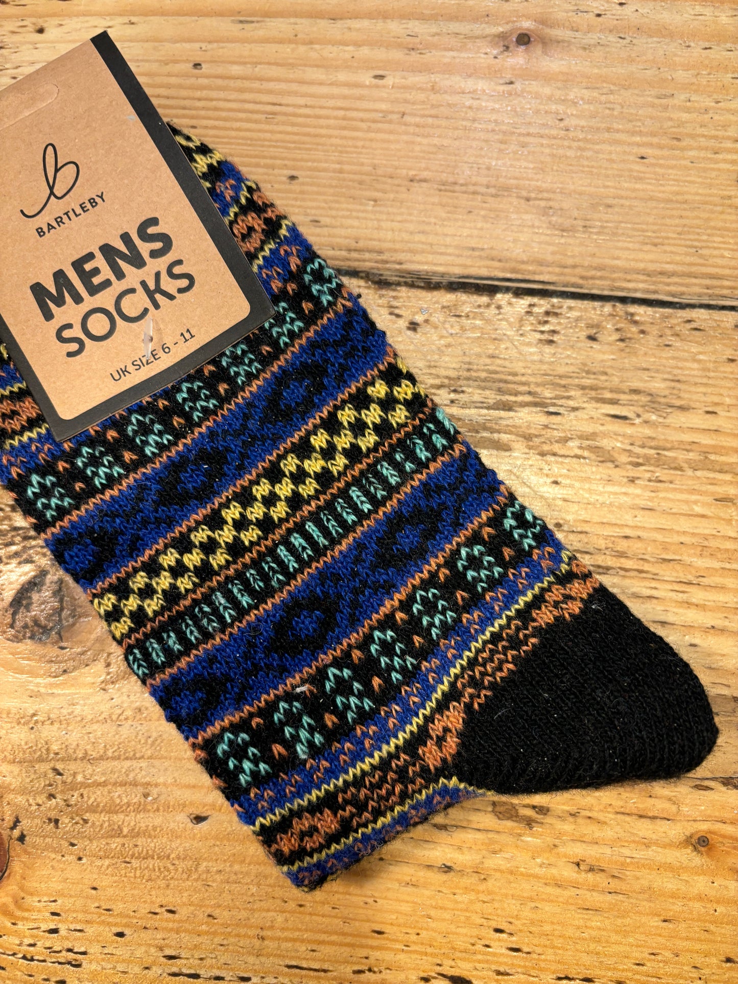 Colorful patterned Bartleby Men’s socks in black, royal blue, and yellow tones on wooden surface