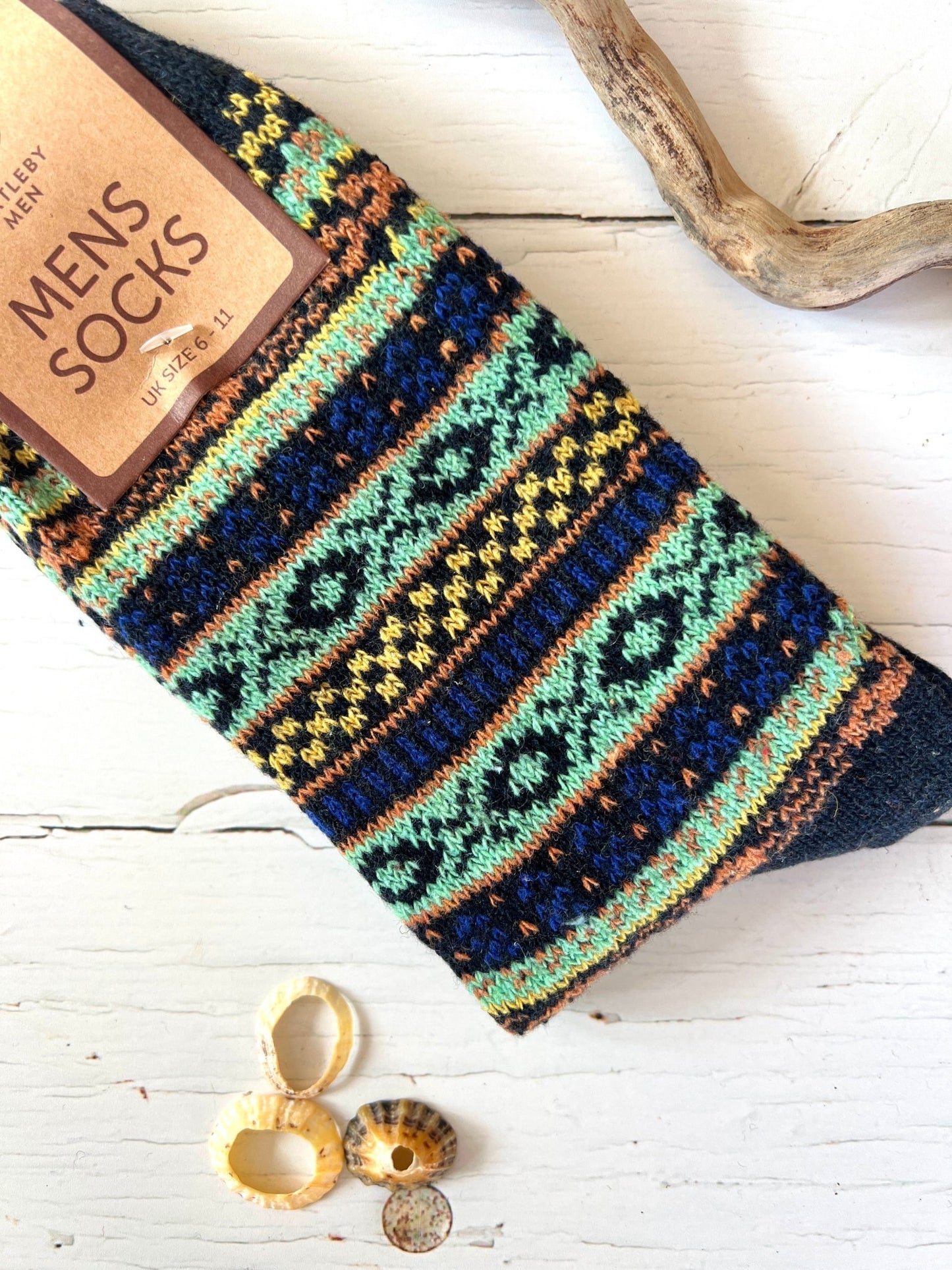 Colorful patterned Bartleby Men’s socks in black, turquoise, and rust tones on white wood with seashells and driftwood