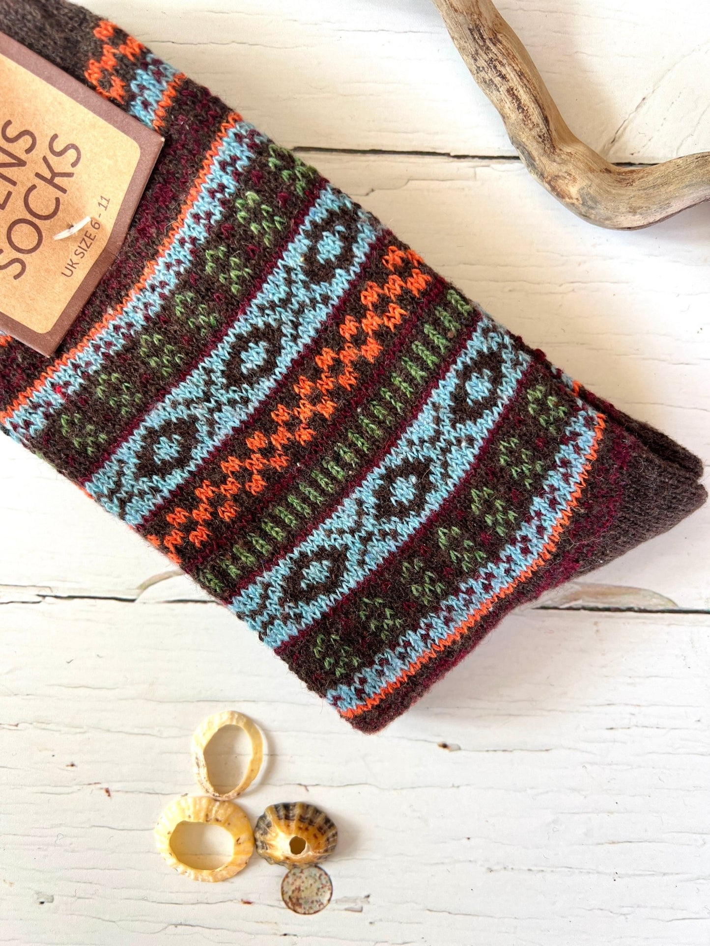 Colorful patterned Bartleby Men’s socks in brown, blue, and orange tones on white wood with seashells and driftwood