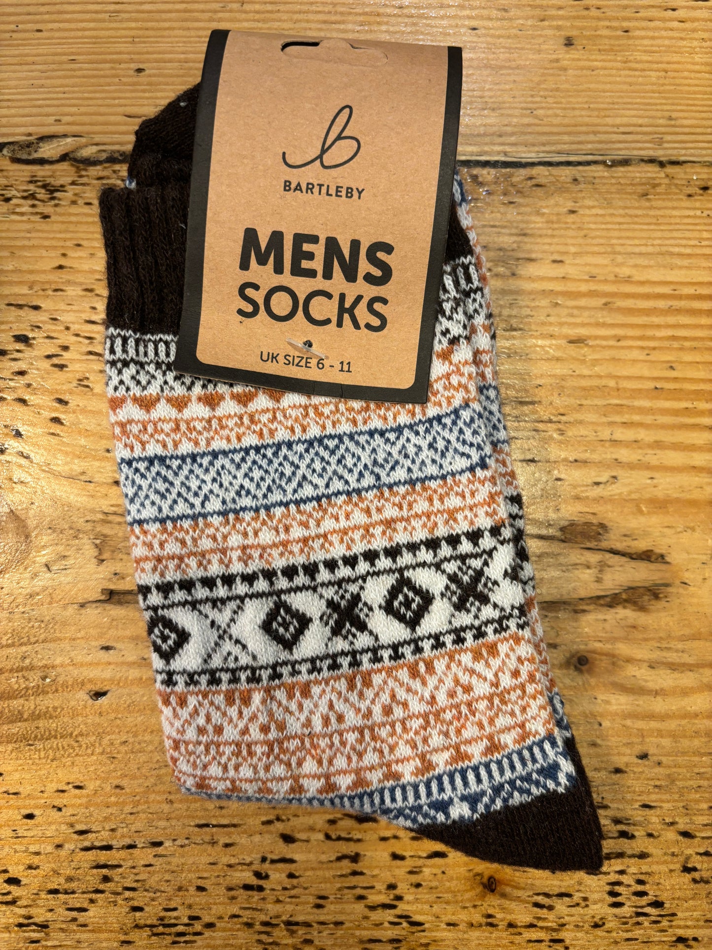 Colorful patterned Bartleby Men’s socks in brown, white, and orange tones on wooden surface