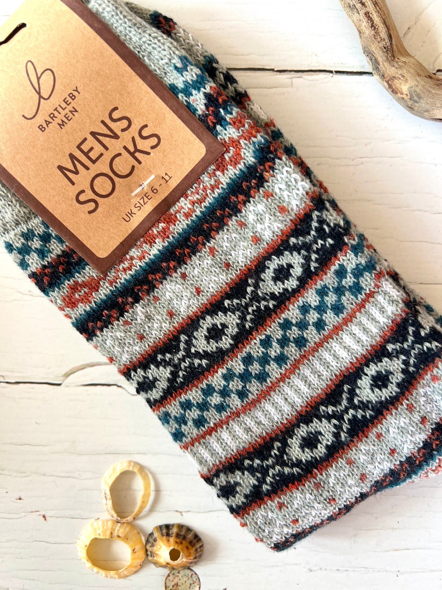 Colorful patterned Bartleby Men’s socks in grey, navy, and teal tones on white wood with seashells and driftwood