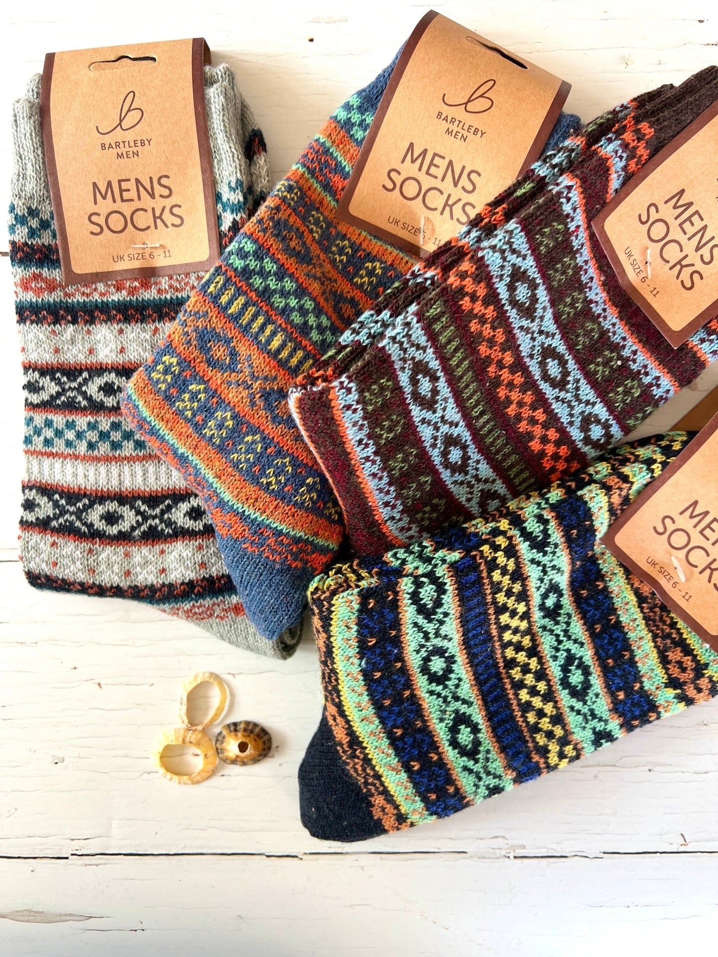Colorful patterned Bartleby Men’s socks in various designs on a white wooden surface, decorated with seashells