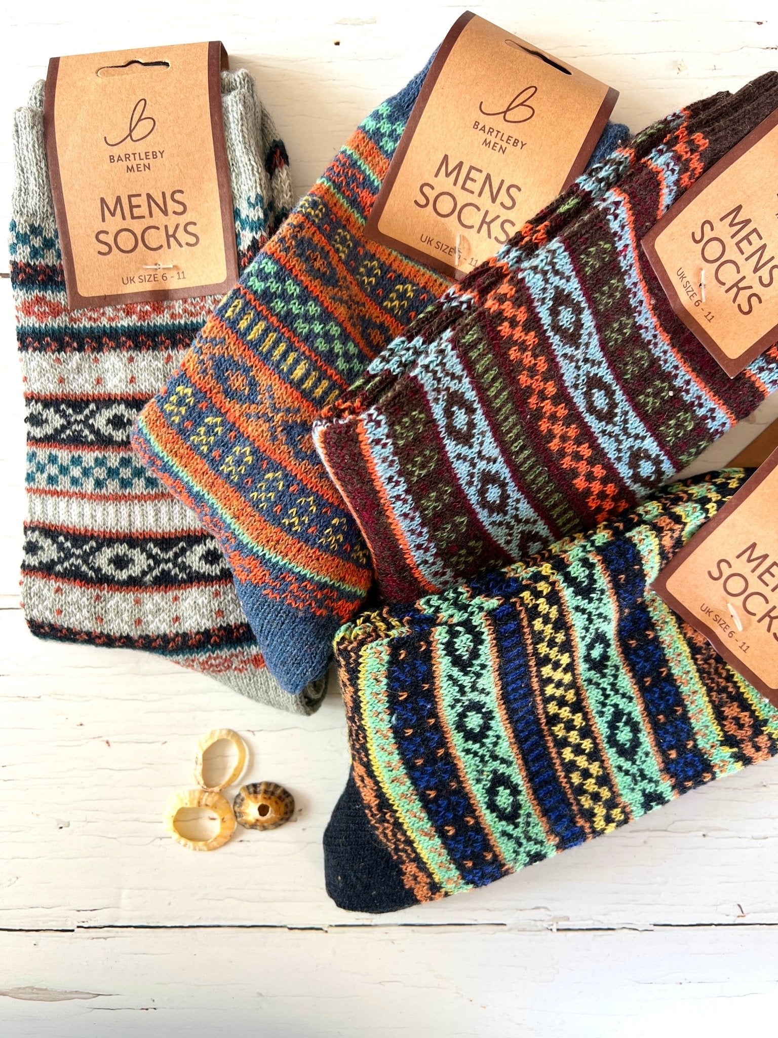 Colorful patterned Bartleby Men’s socks in various designs on a white wooden surface, decorated with seashells