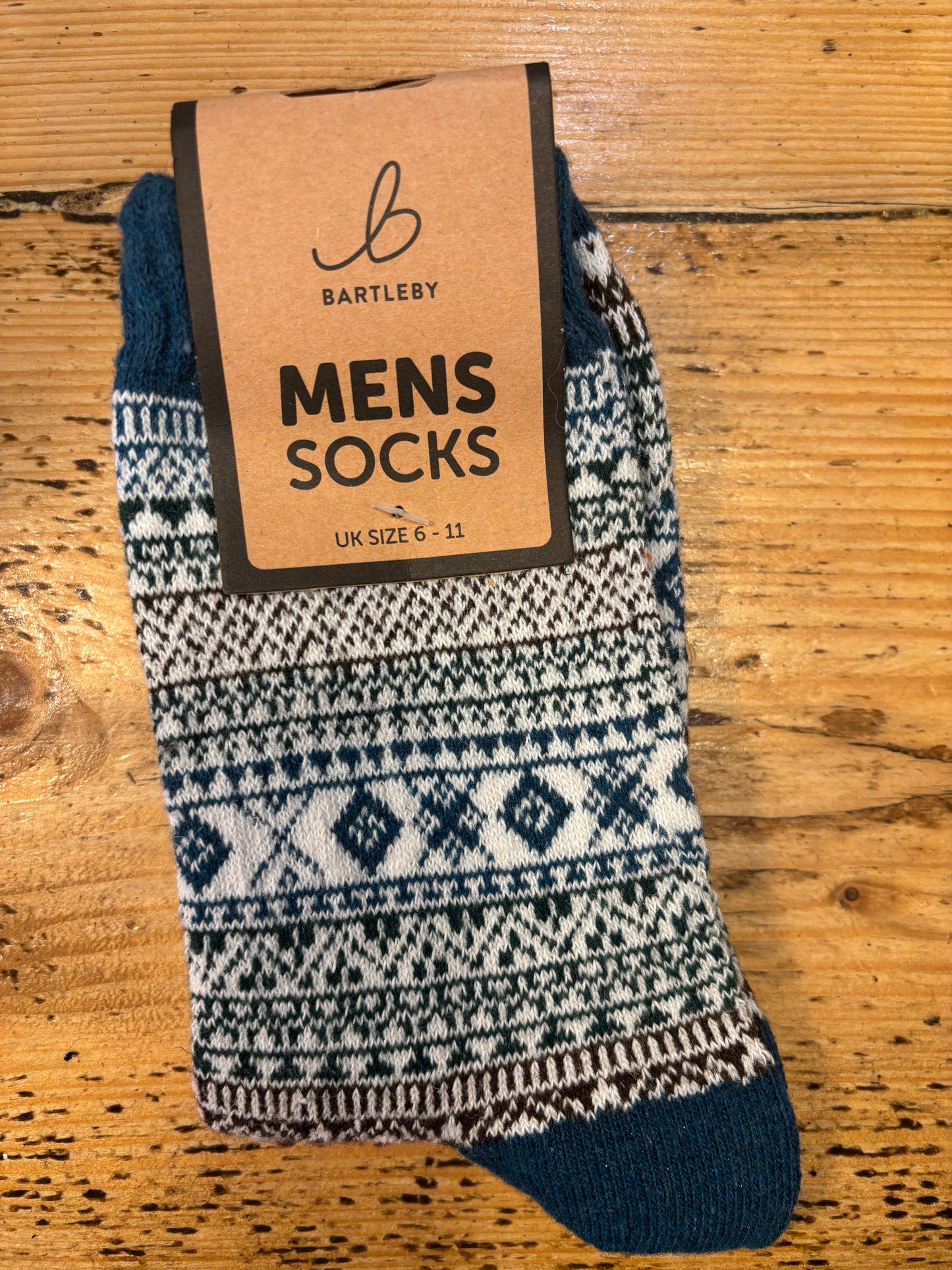 Colorful patterned Bartleby Men’s socks in teal, white, and green tones on wooden surface