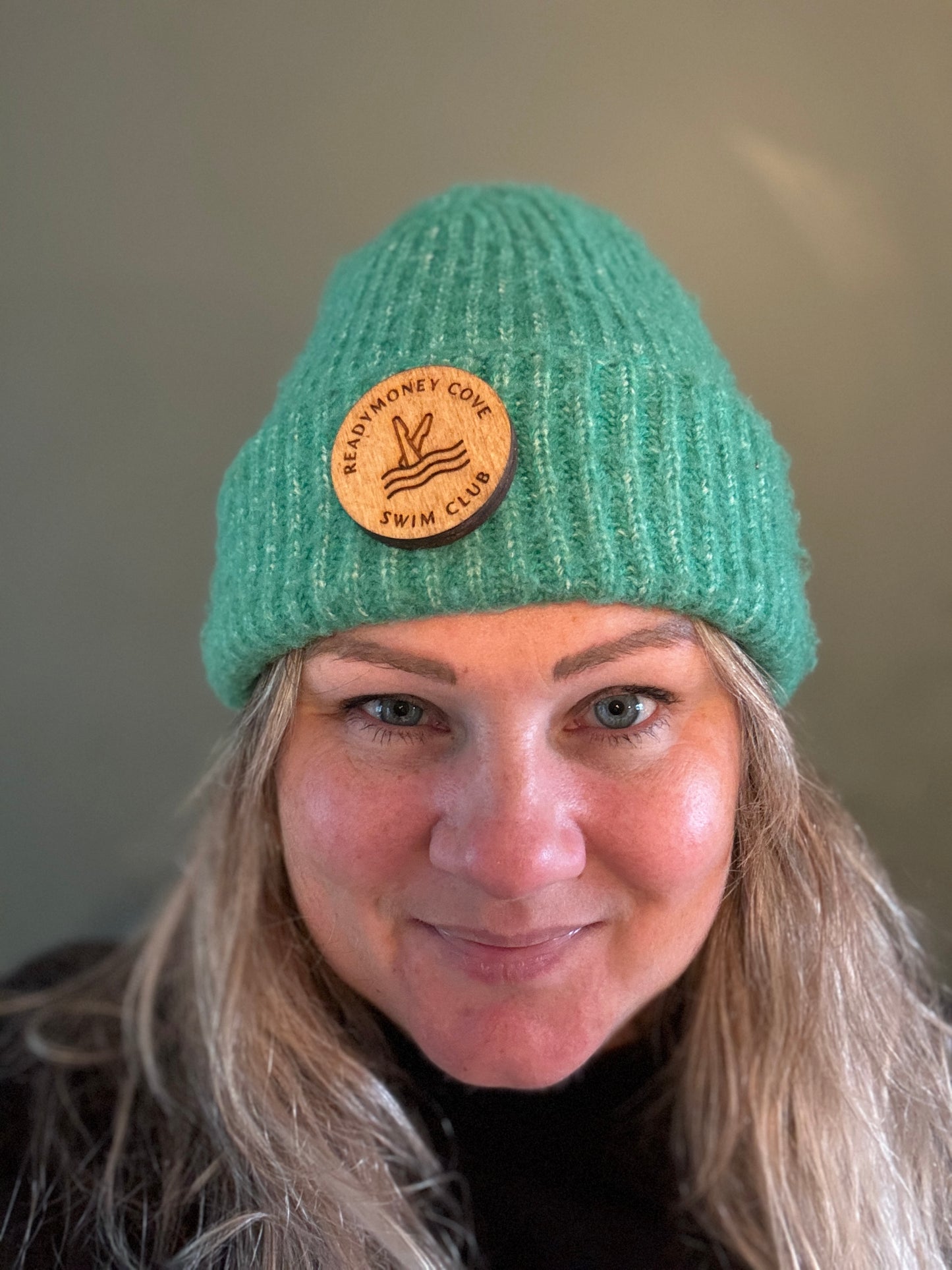 wooden 'Readymoney Cove Swim Club' circular badge pin worn on a green knitted beanie nautical, coastal souvenir, winter hat accessory