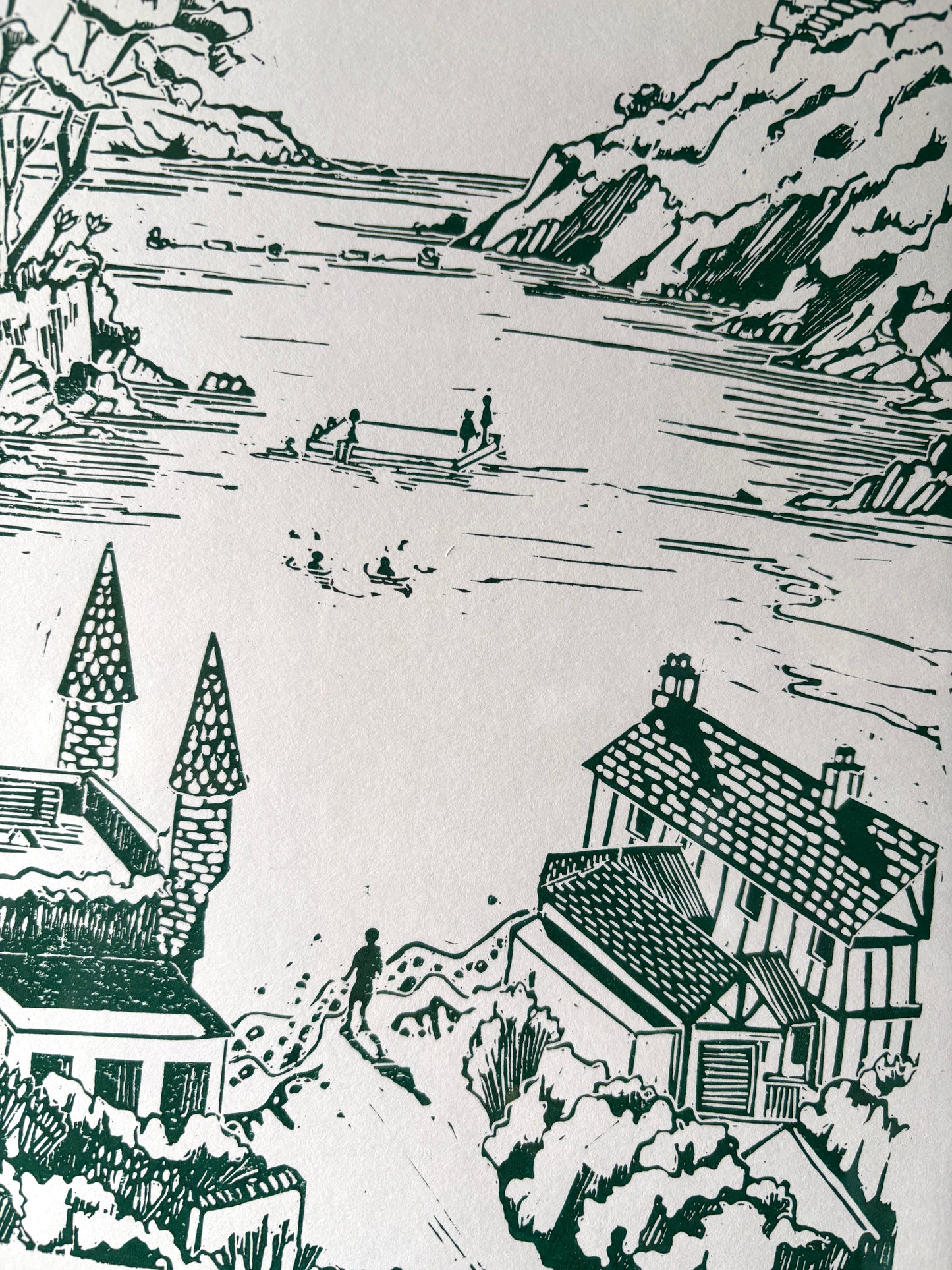closeup shot of a detailed linocut print showing a Cornish bay, cottages, and sea activity. Original green coastal wall art