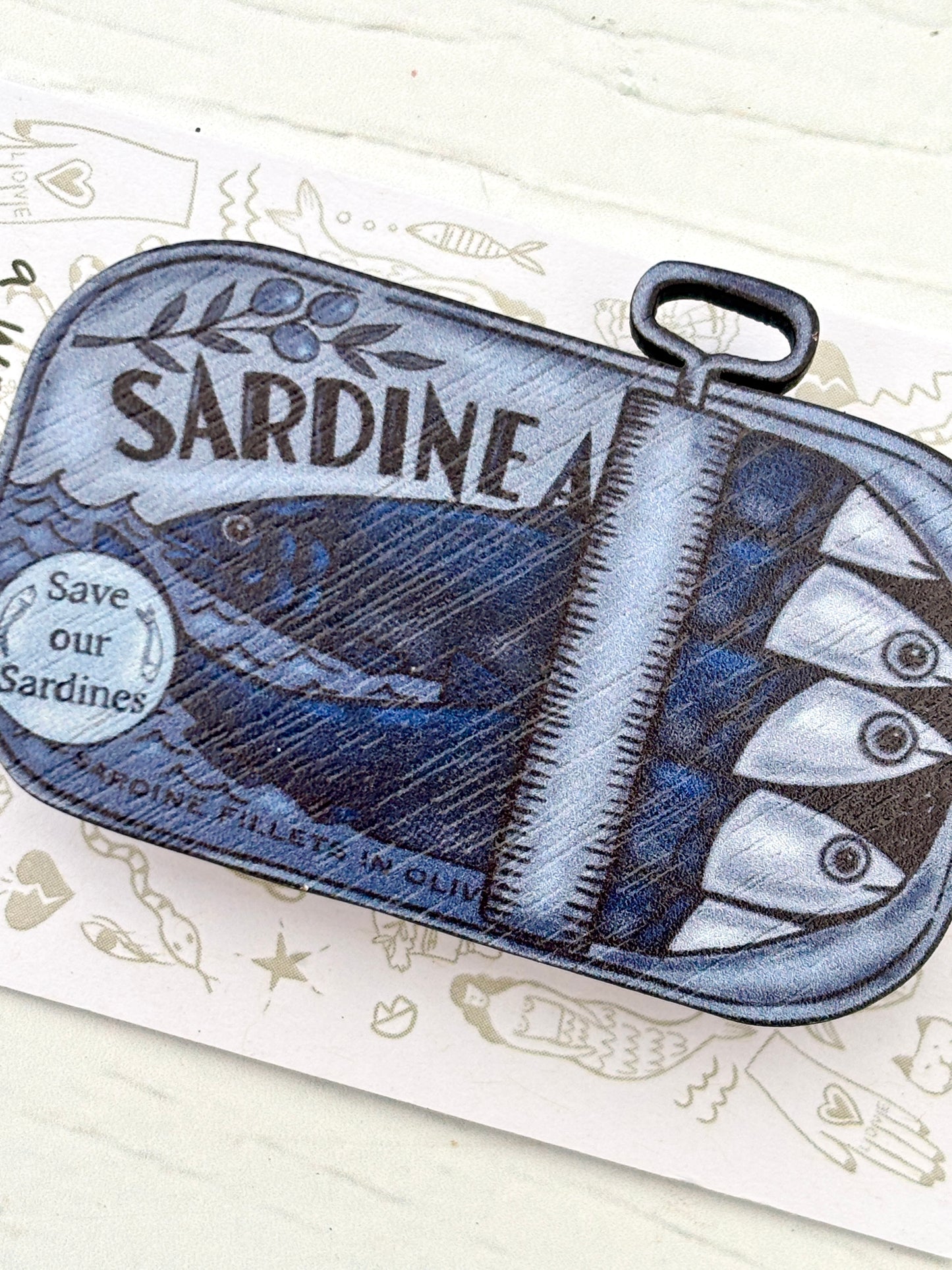closeup shot of tin of sardines wooden pin—eco-friendly nautical badge with quirky fish tin design for ocean lovers and coastal gifting