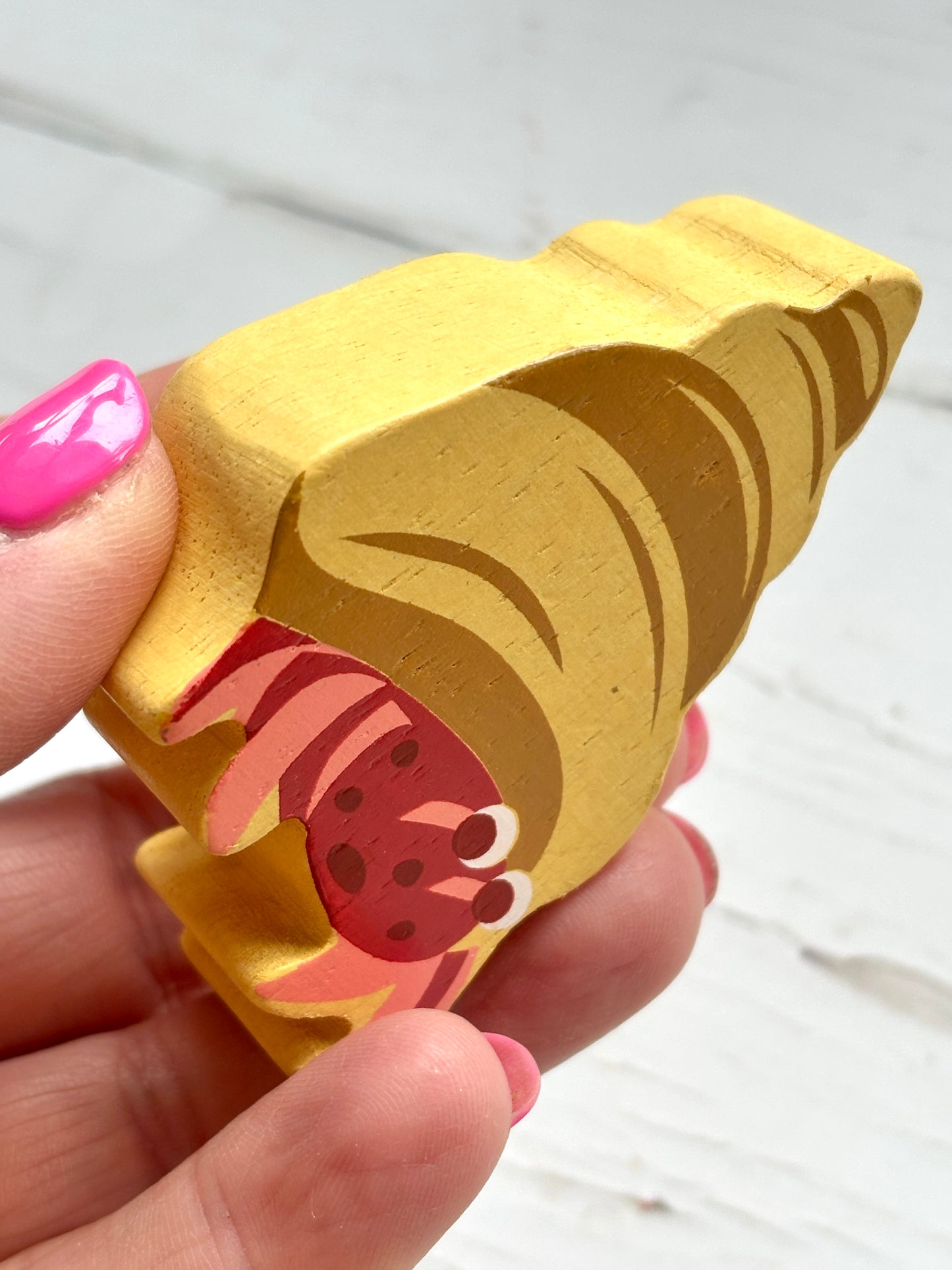 side view of wooden hermit crab toy with spiral shell, hand-painted beach decor for ocean-themed play