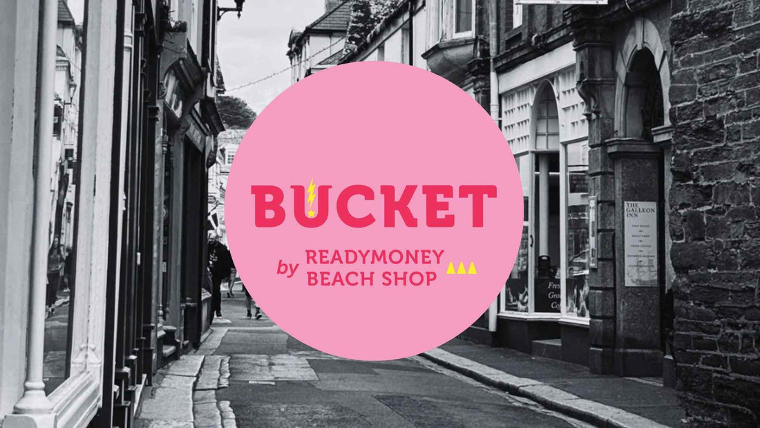 the bright pink logo of Bucket by Readymoney Beach Shop against a black and white photo of Fowey's Fore Street