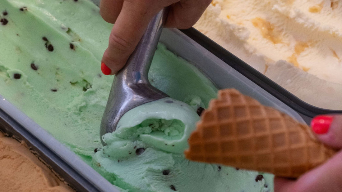 A picture of a hand scooping a mint choc choc ice cream into a cone