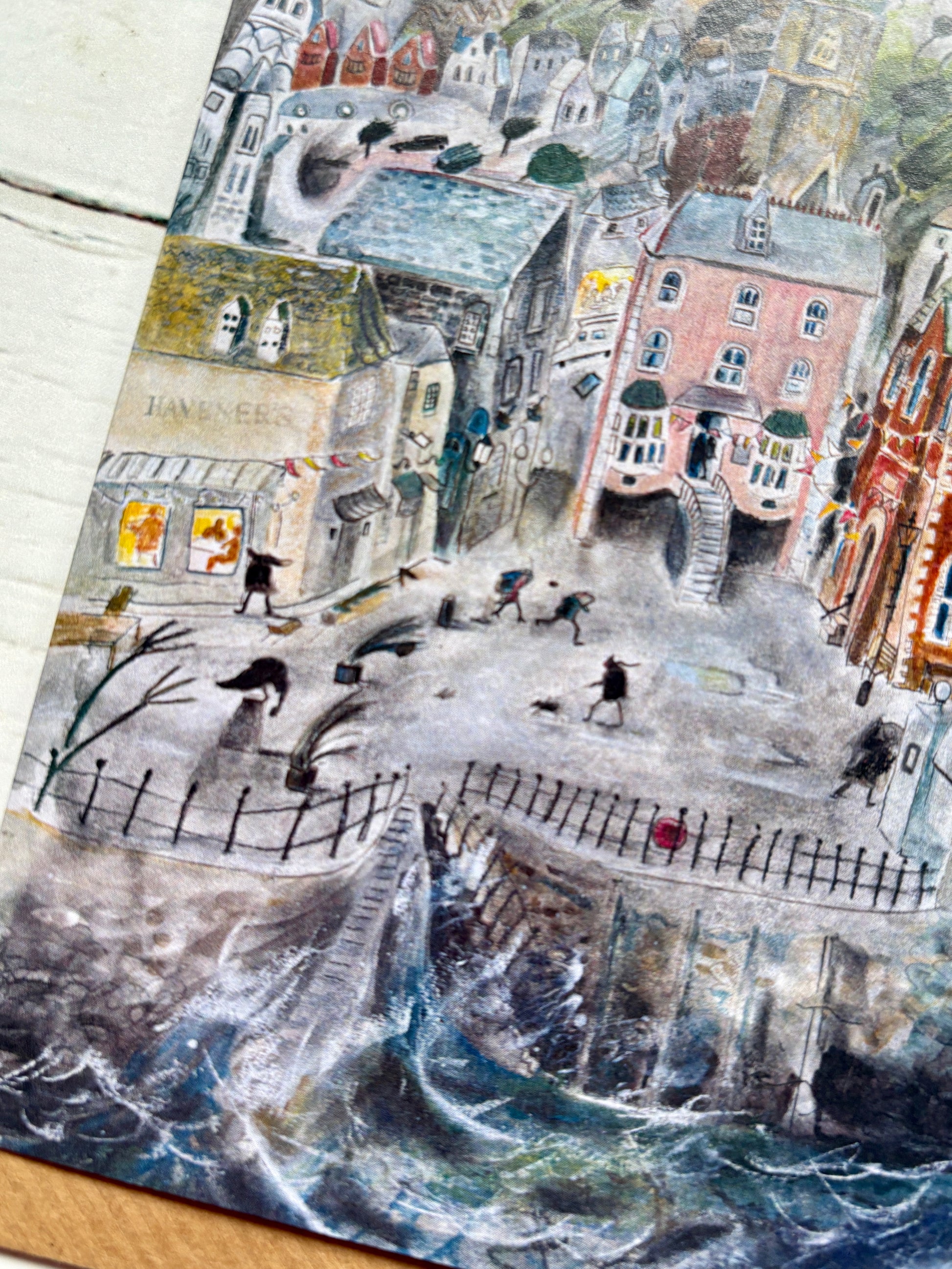 lifestyle shot—stormy seaside card with pastel town, swirling waves, and cozy coastal vibes for ocean-inspired gifting