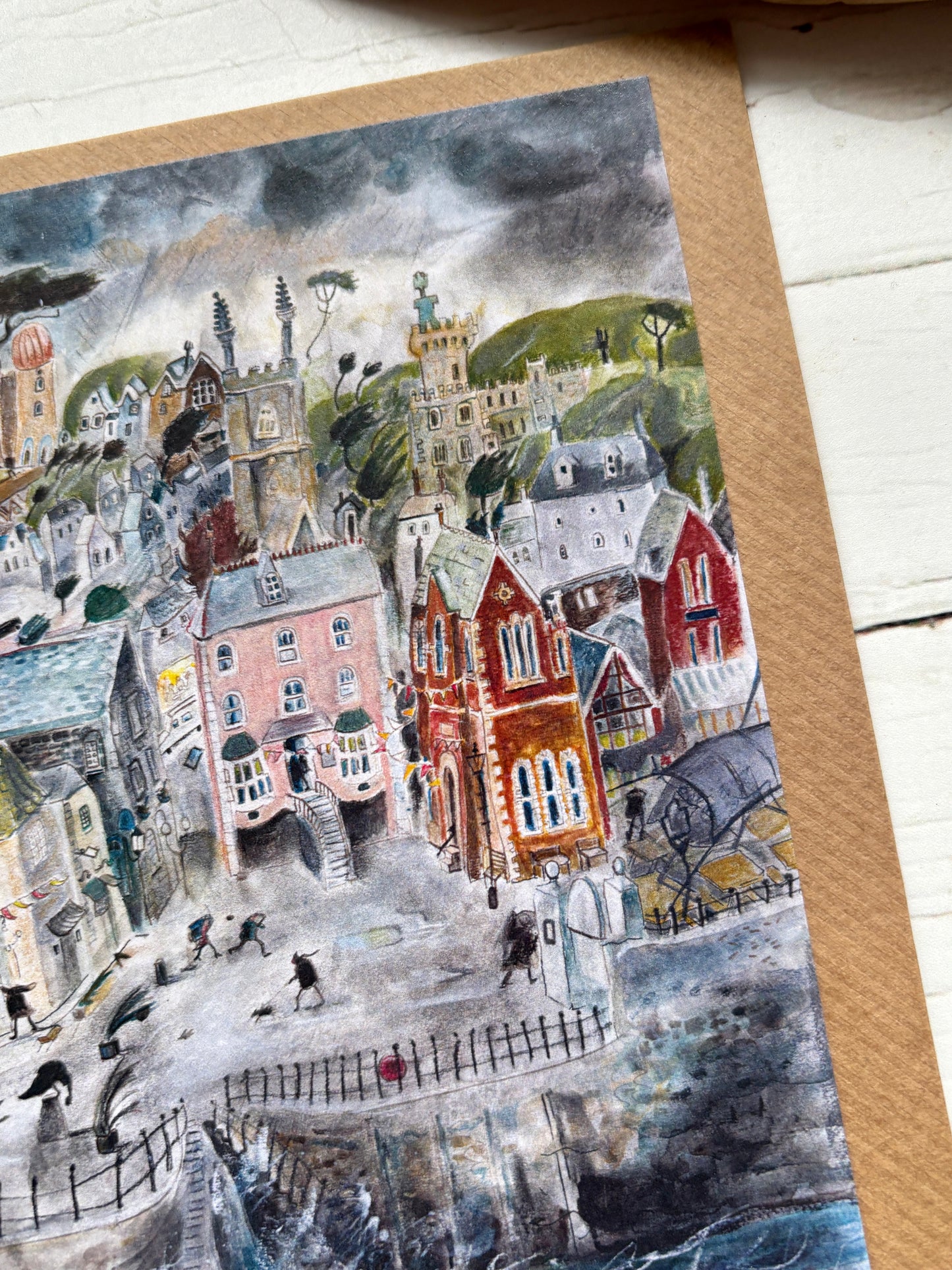 lifestyle shot—stormy seaside card with pastel town, crashing waves, and moody sky for coastal art and ocean lovers