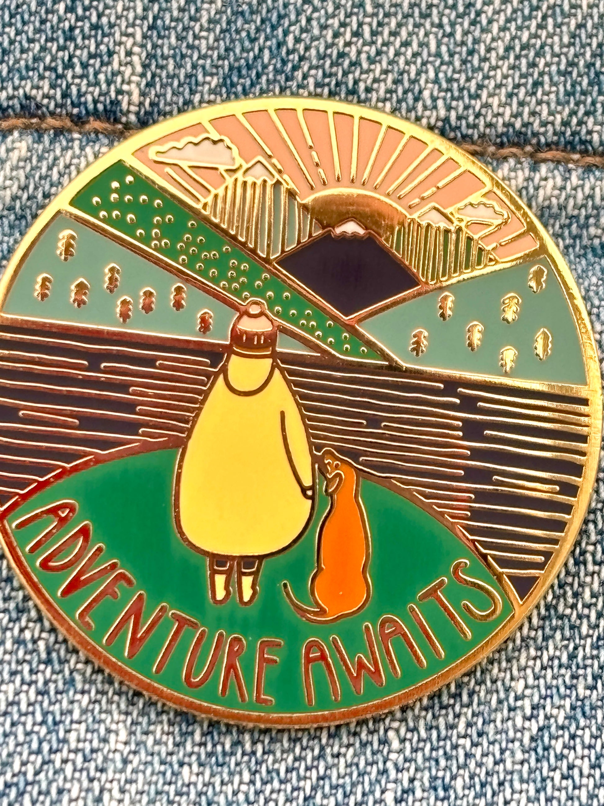 adventure awaits pin detail, hiker silhouette with dog, layered enamel mountains, gold finish, outdoor badge jewelry