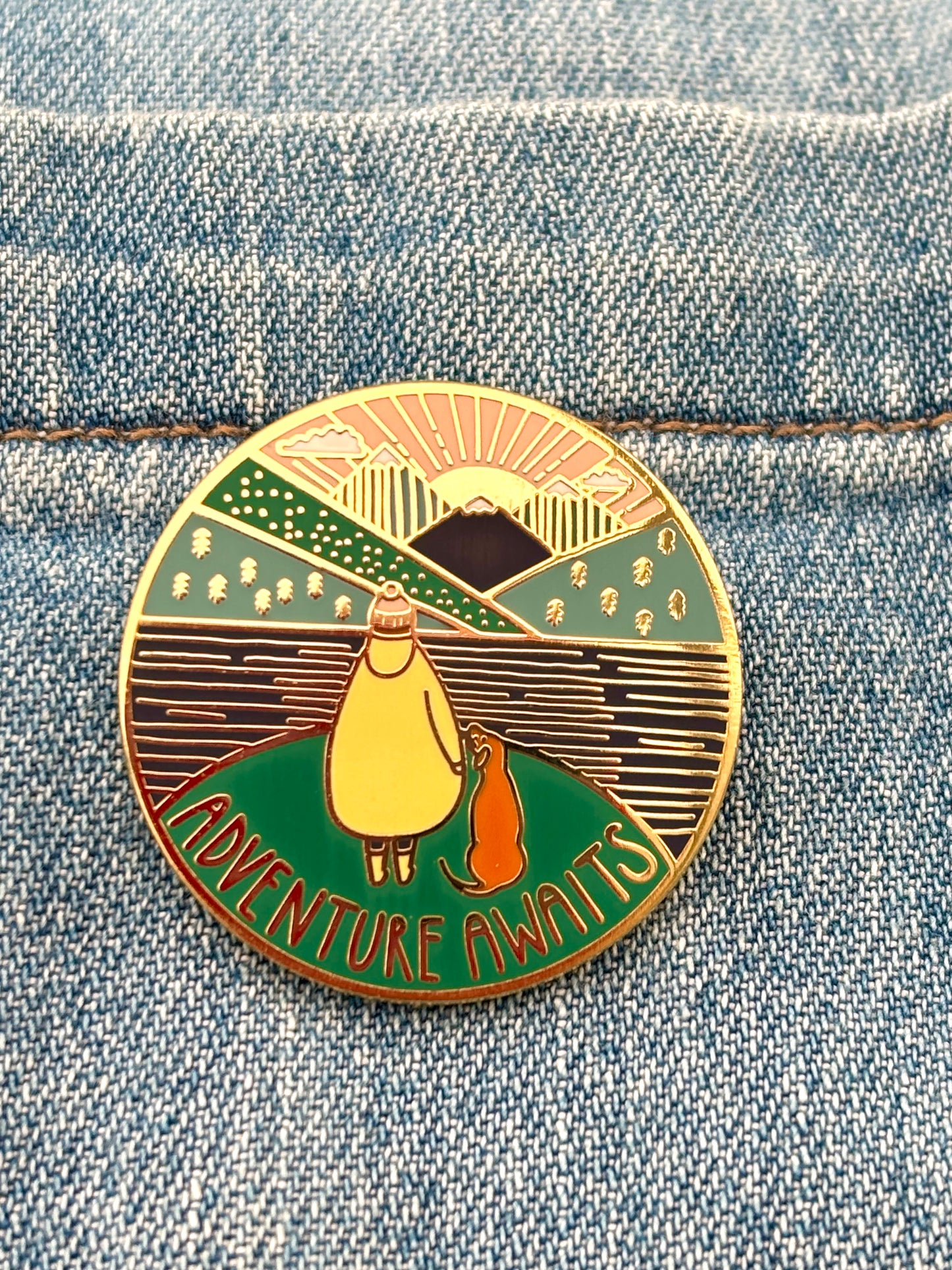 adventure awaits enamel pin on denim jacket, hiking badge with dog walker, mountain scene, outdoor accessory