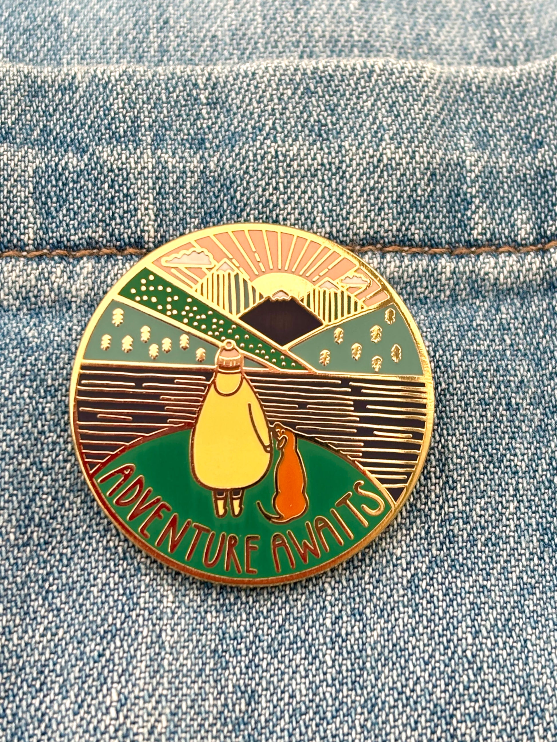 adventure awaits enamel pin on denim jacket, hiking badge with dog walker, mountain scene, outdoor accessory