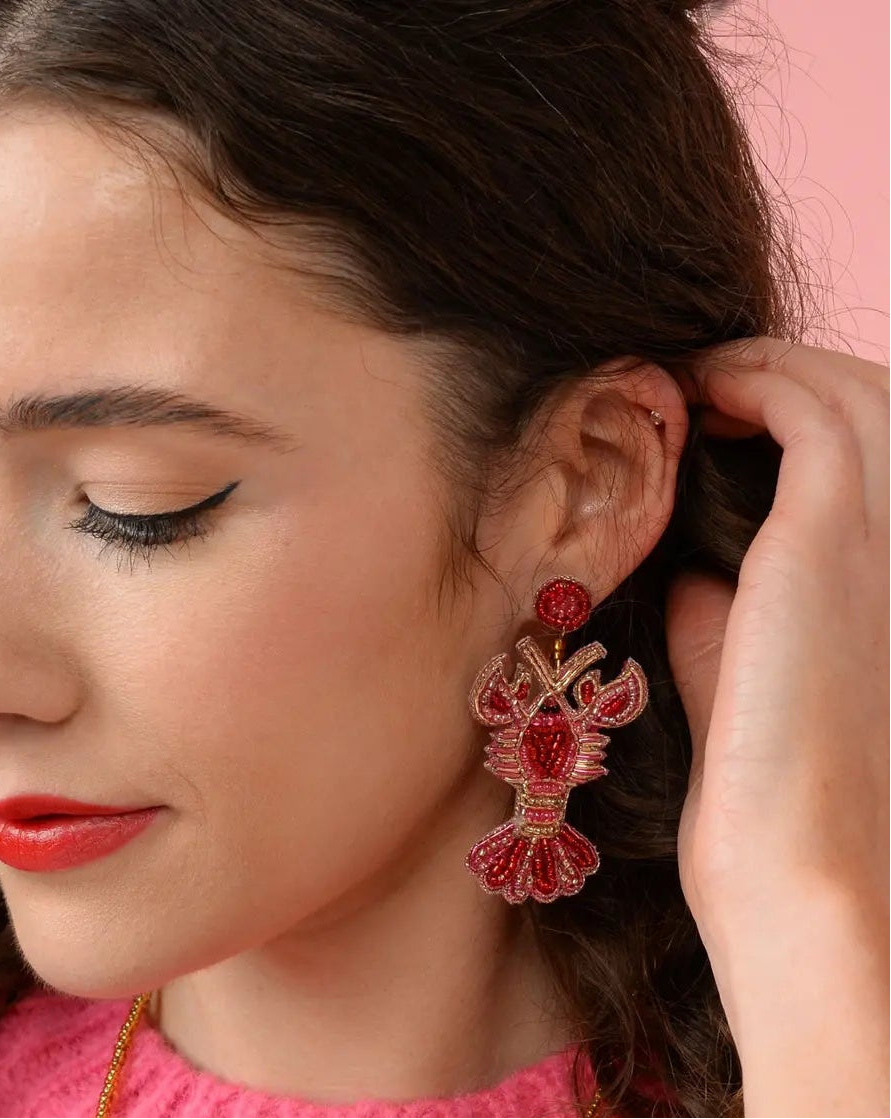 Woman wearing red beaded lobster earrings against a pink background