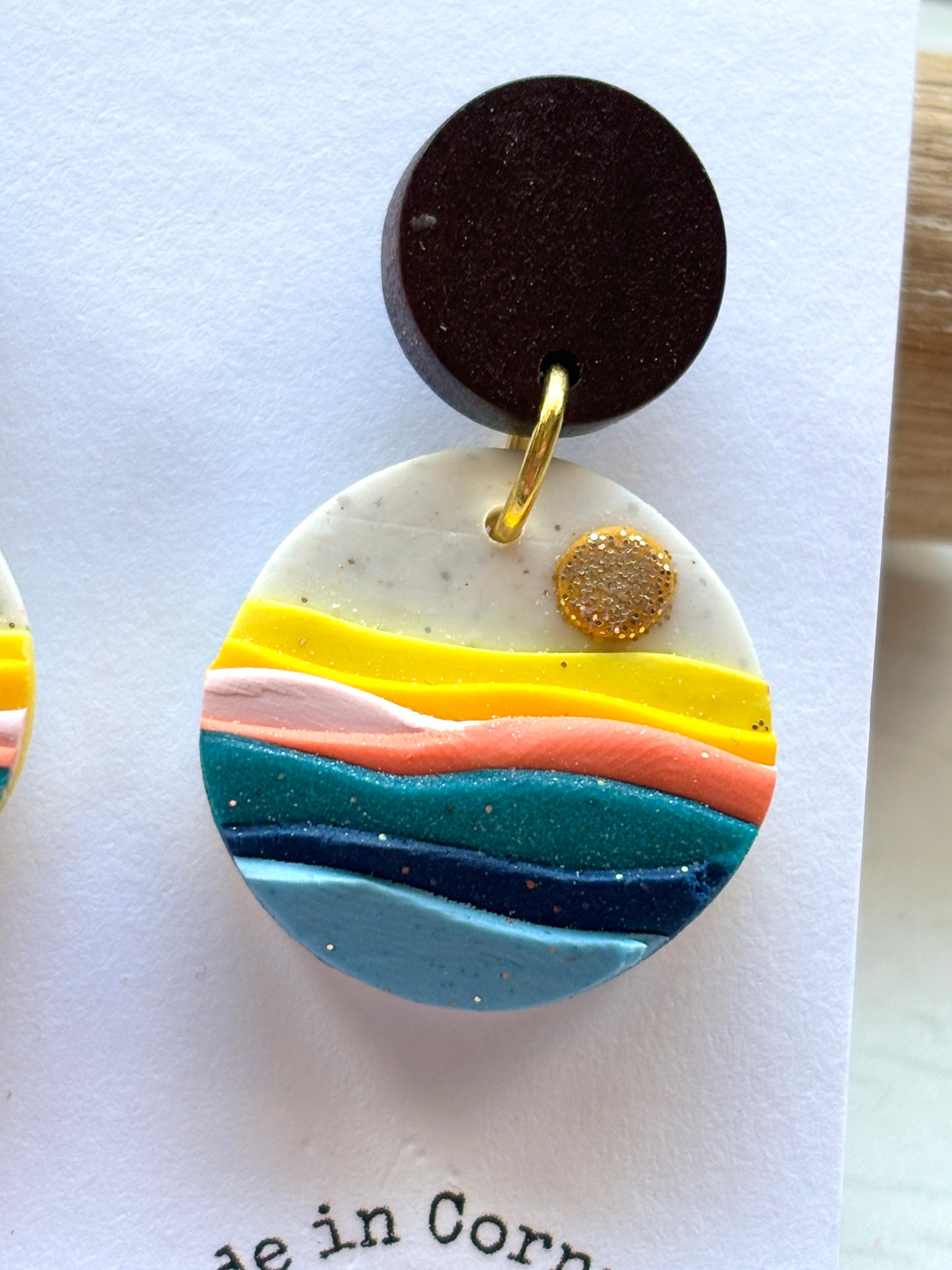 closeup shot of polymer resin beach sunset earrings layered coastal design with orange, pink, and teal waves handmade beach accessory
