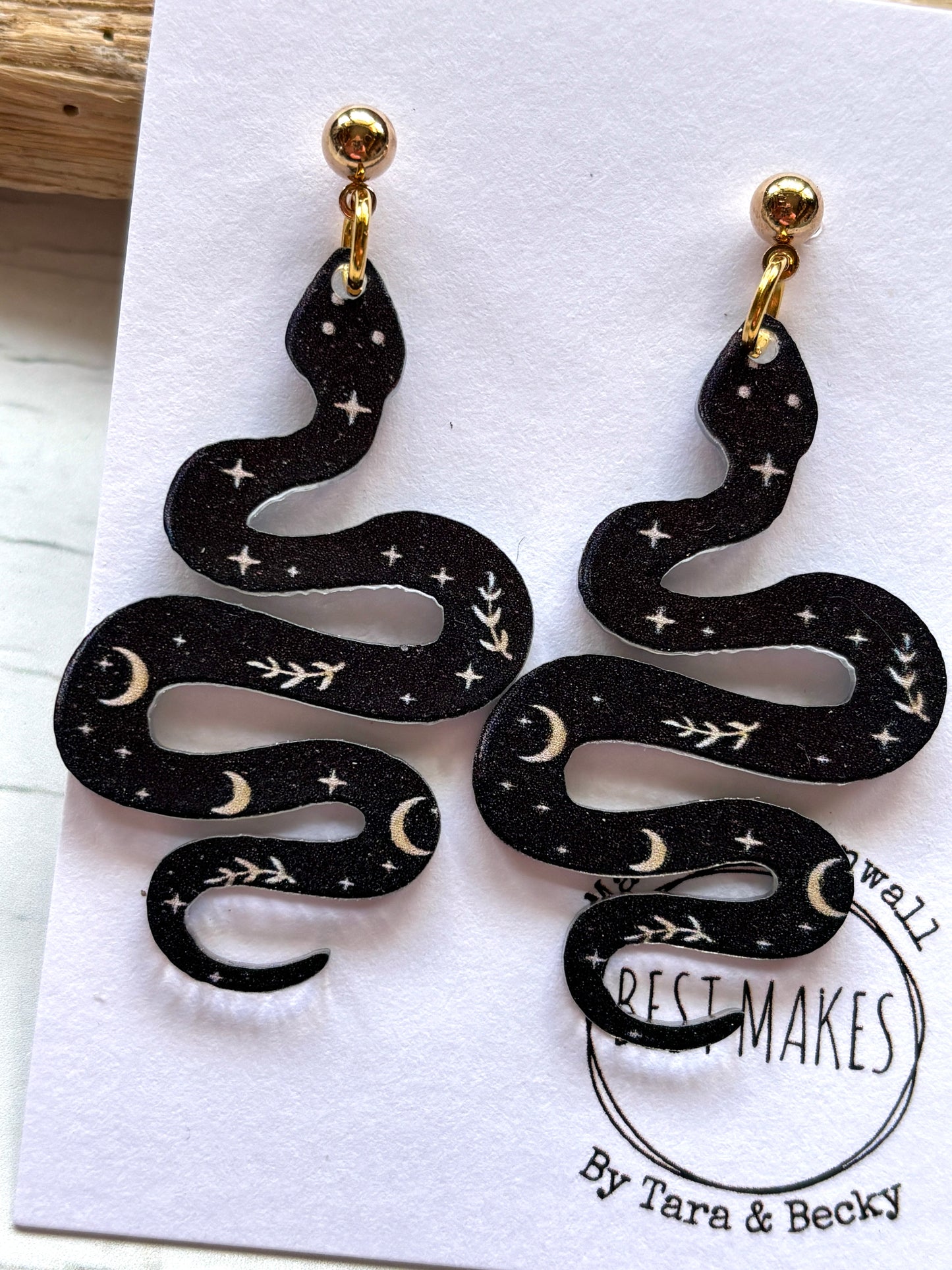 closeup shot of black polymer resin snake earrings witchy celestial jewelry with moon and star print gothic serpent fashion accessories