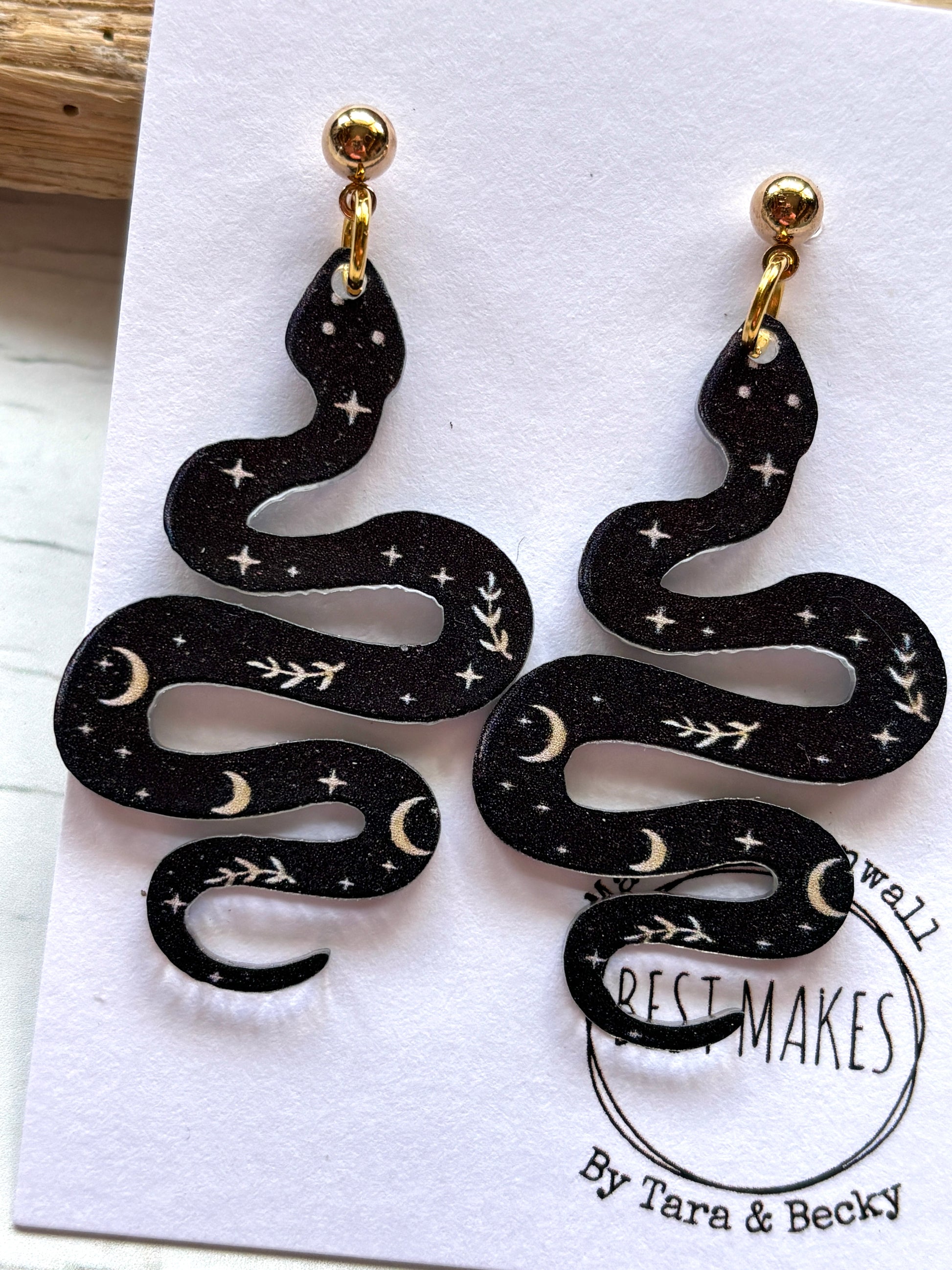 closeup shot of black polymer resin snake earrings witchy celestial jewelry with moon and star print gothic serpent fashion accessories