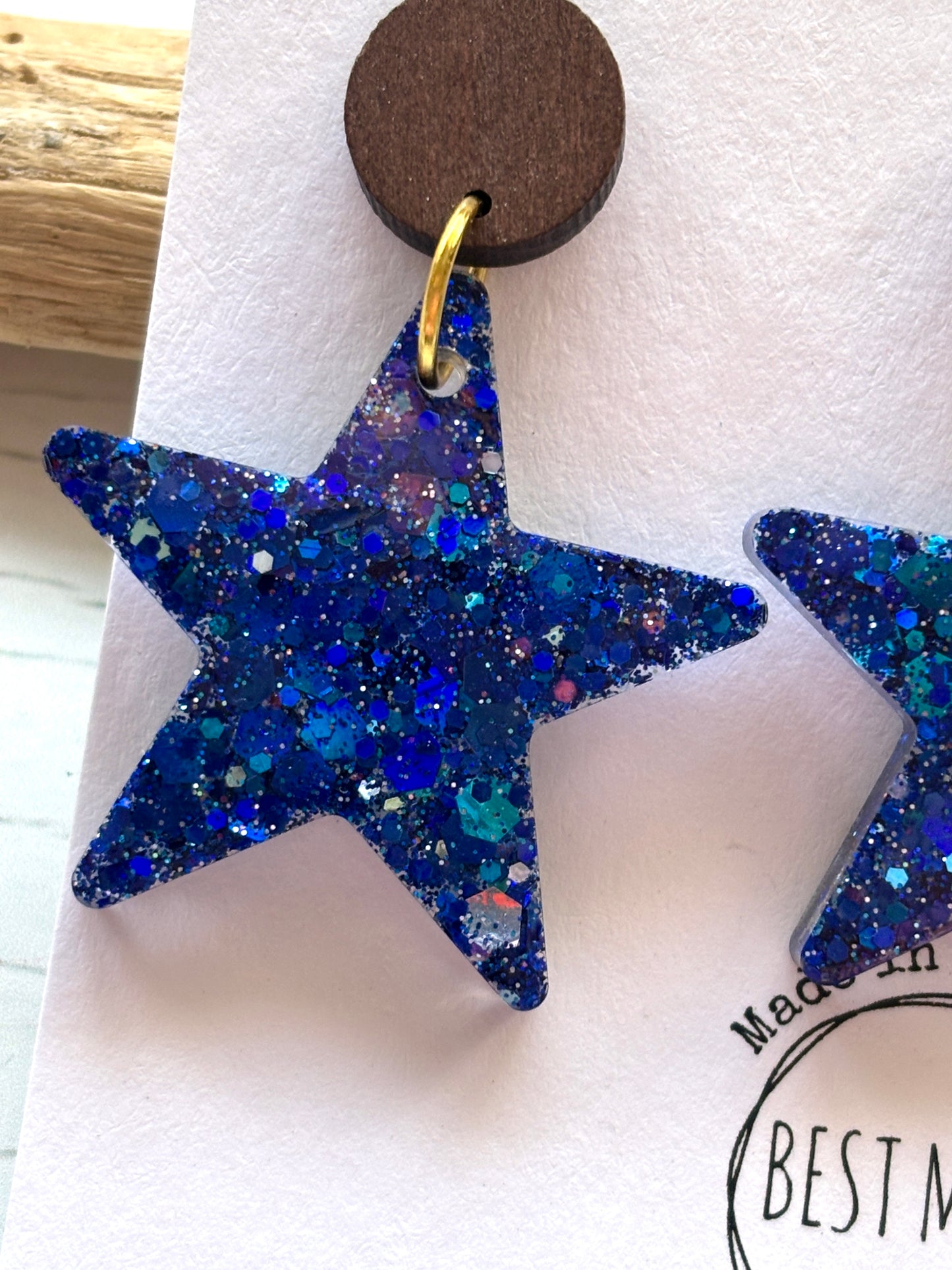 closeup shot of blue resin glitter star earrings statement jewelry with dark wooden stud celestial galaxy fashion and handmade gift