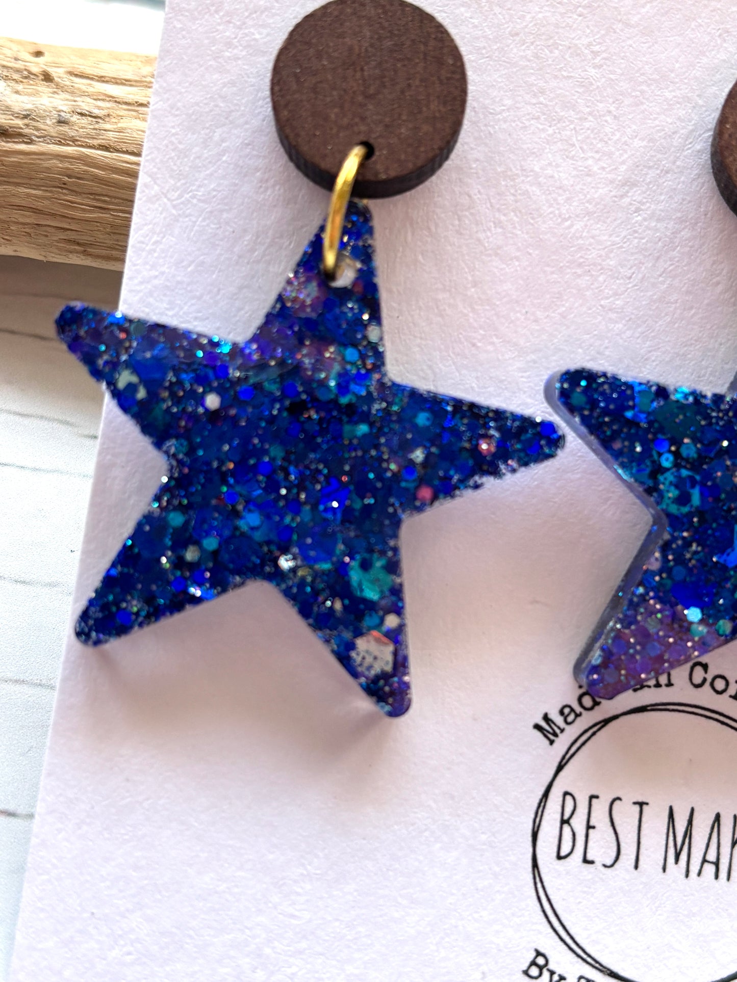closeup shot of blue resin glitter star earrings statement jewelry with dark wooden stud celestial galaxy fashion and handmade gift