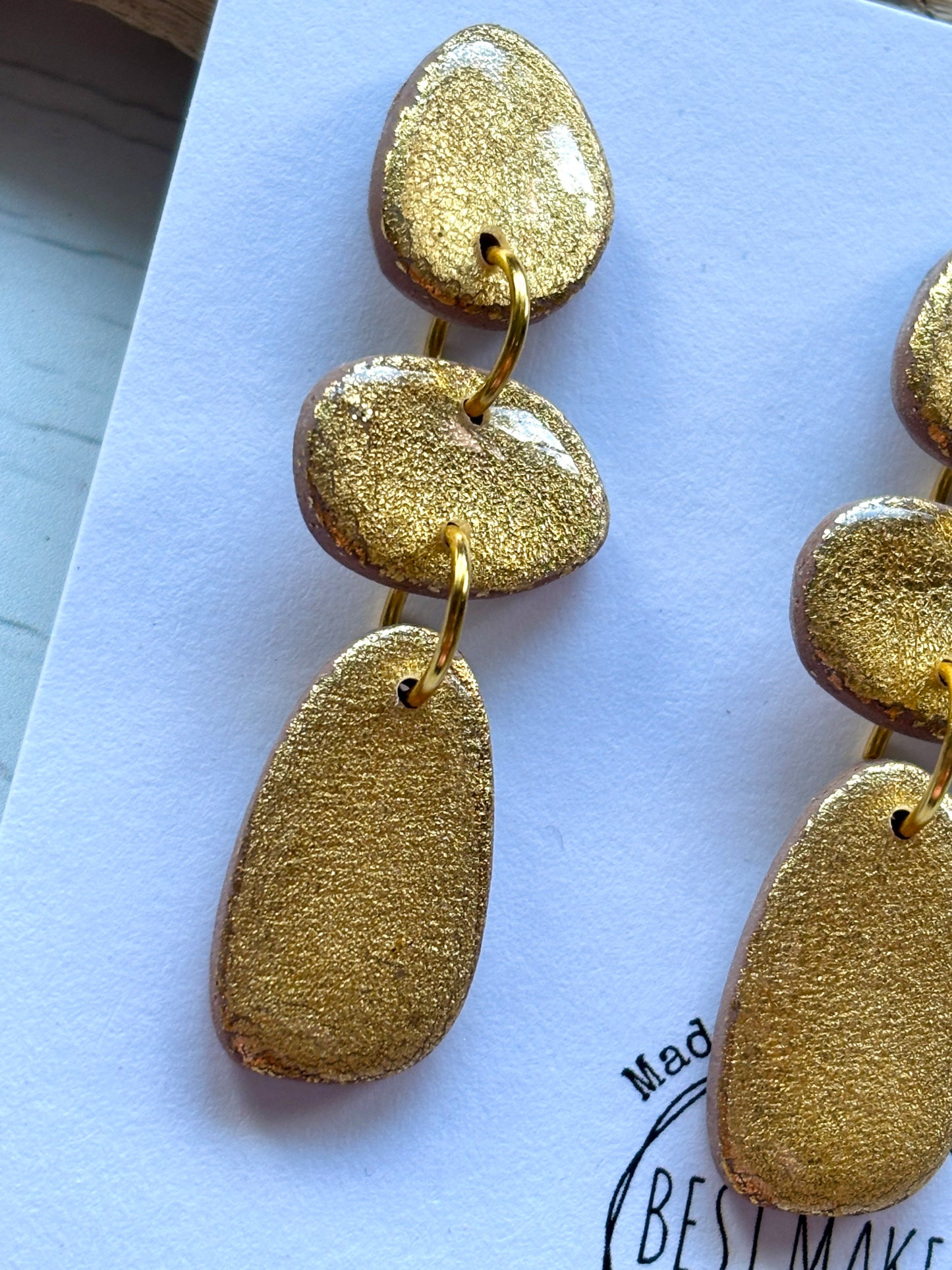closeup shot of gold nugget drop earrings shiny polymer resin with a textured metallic finish handmade tiered statement jewelry