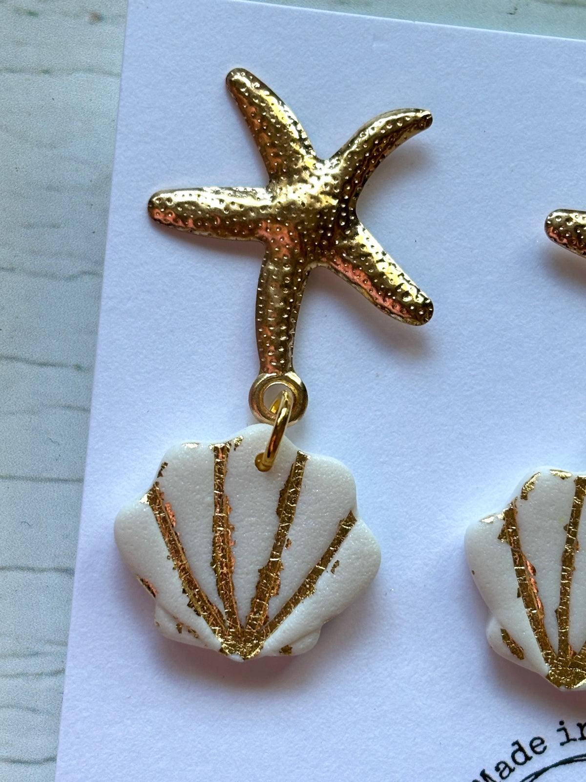 closeup shot of gold starfish earring stud connected to a white seashell dangle handmade polymer resin and gold-tone jewelry