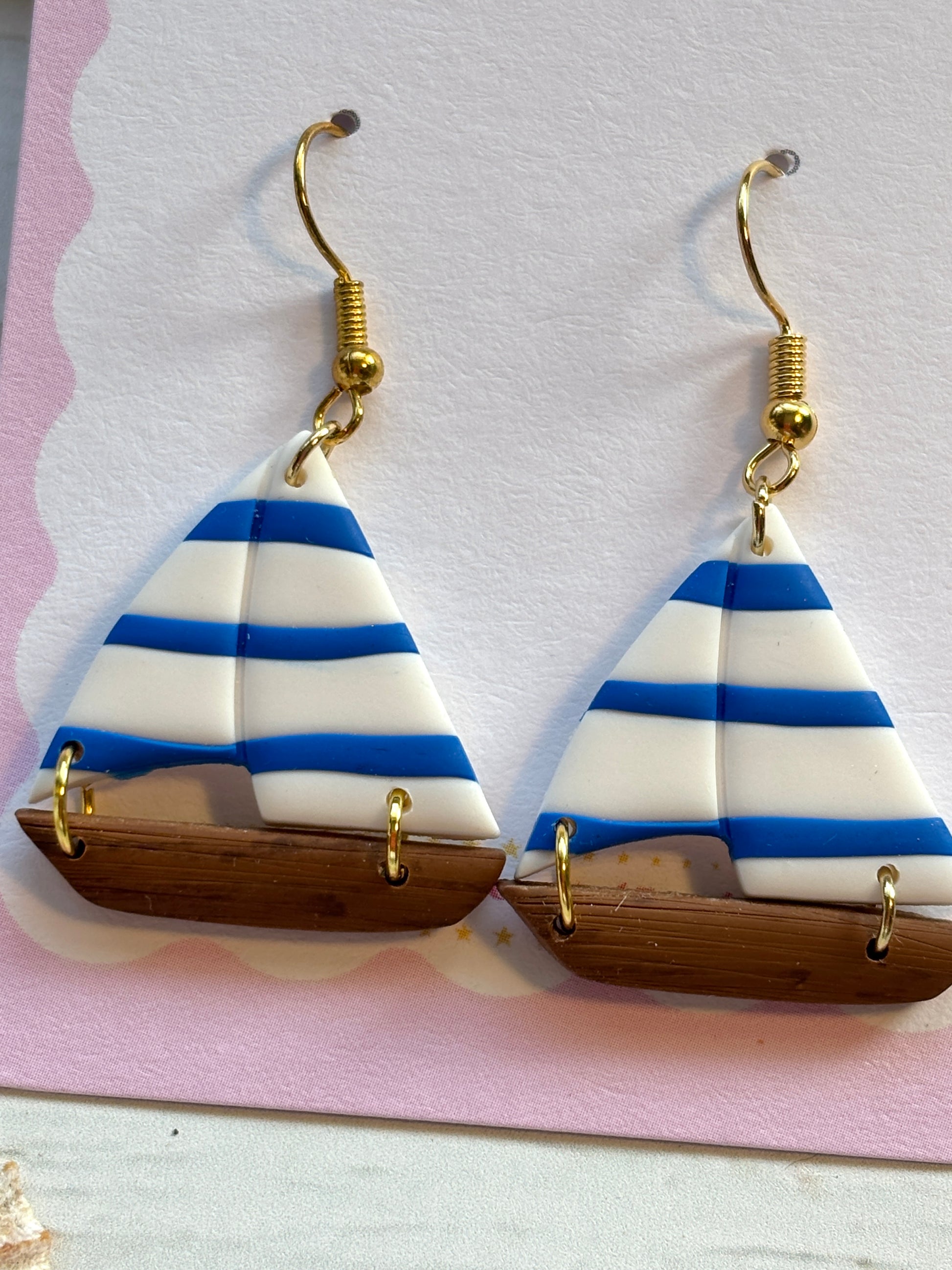closeup shot of striped sailboat drop earrings handcrafted polymer clay summer nautical jewelry gold hook dangle earrings